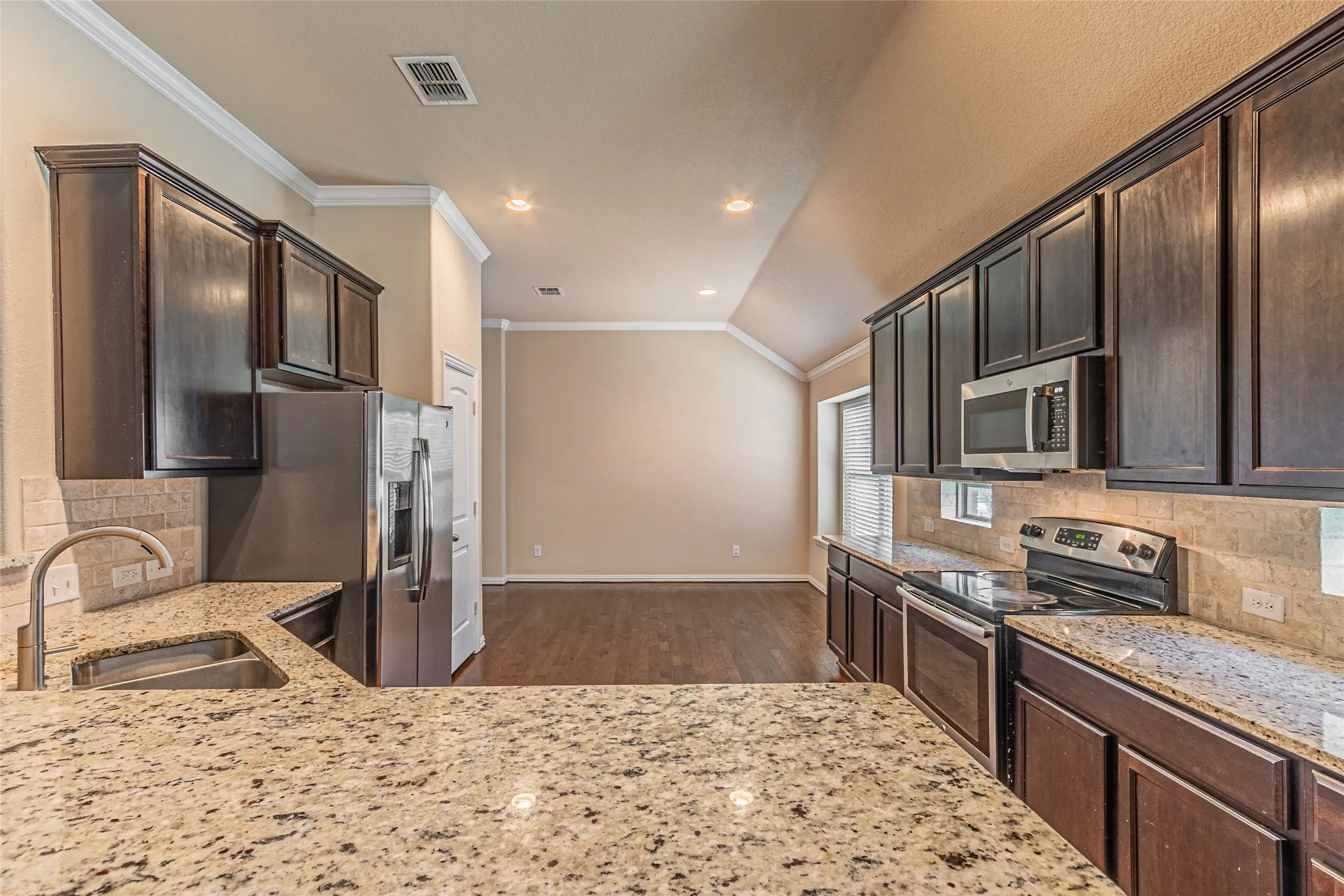 Kitchen featuring dark wood cabinetry, stone countertops, stainless steel appliances, a subway tile backsplash, and wood-finish flooring