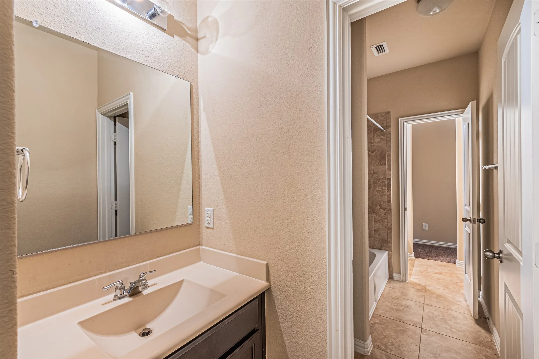 Vanity with integrated sink, chrome hardware, wall-mounted mirror, and tile flooring
