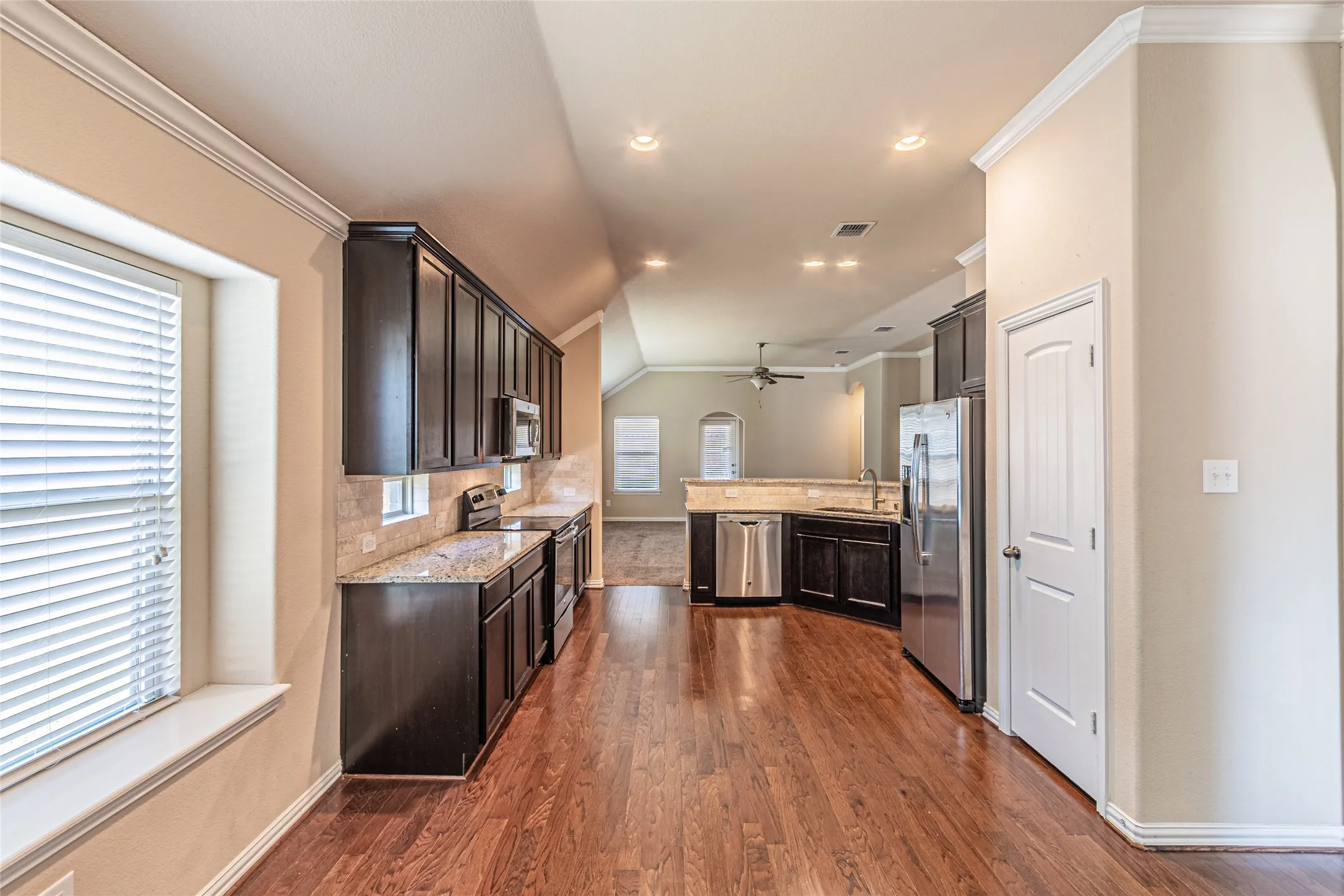 Kitchen featuring dark-finish cabinetry, stone-surface countertops, stainless steel appliances, and wood-finish flooring with crown molding