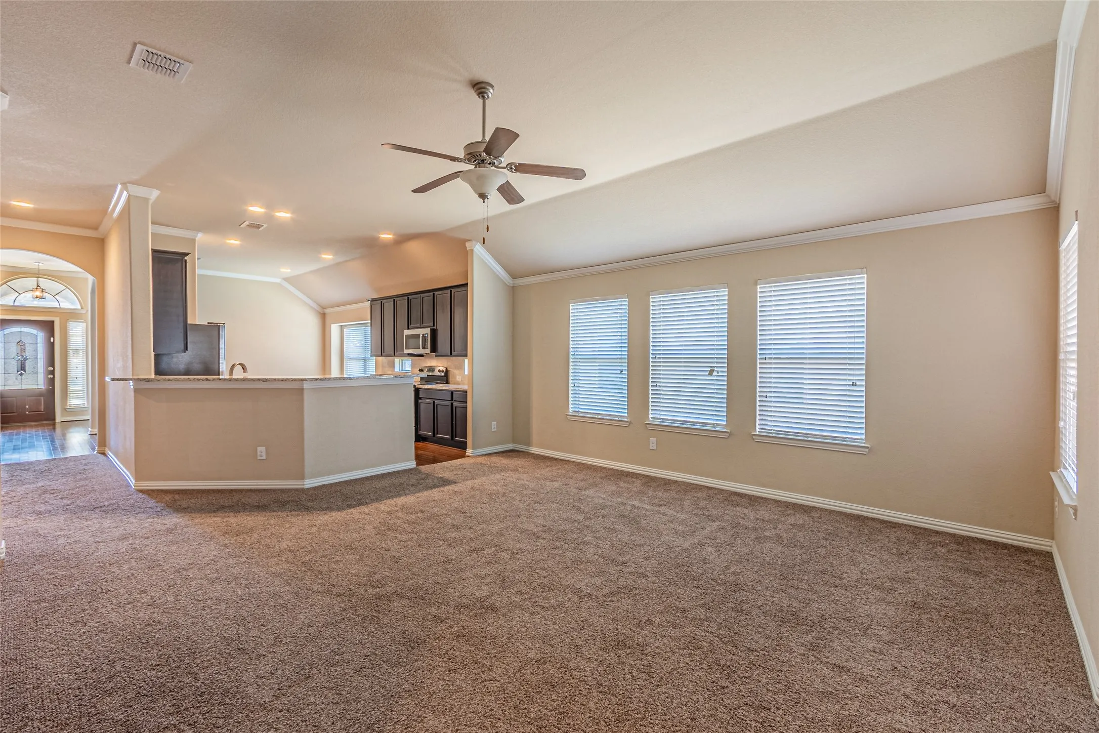 Vaulted ceilings, recessed lighting, ceiling fan, and kitchen featuring dark-tone cabinetry and an island with a stone-finish countertop