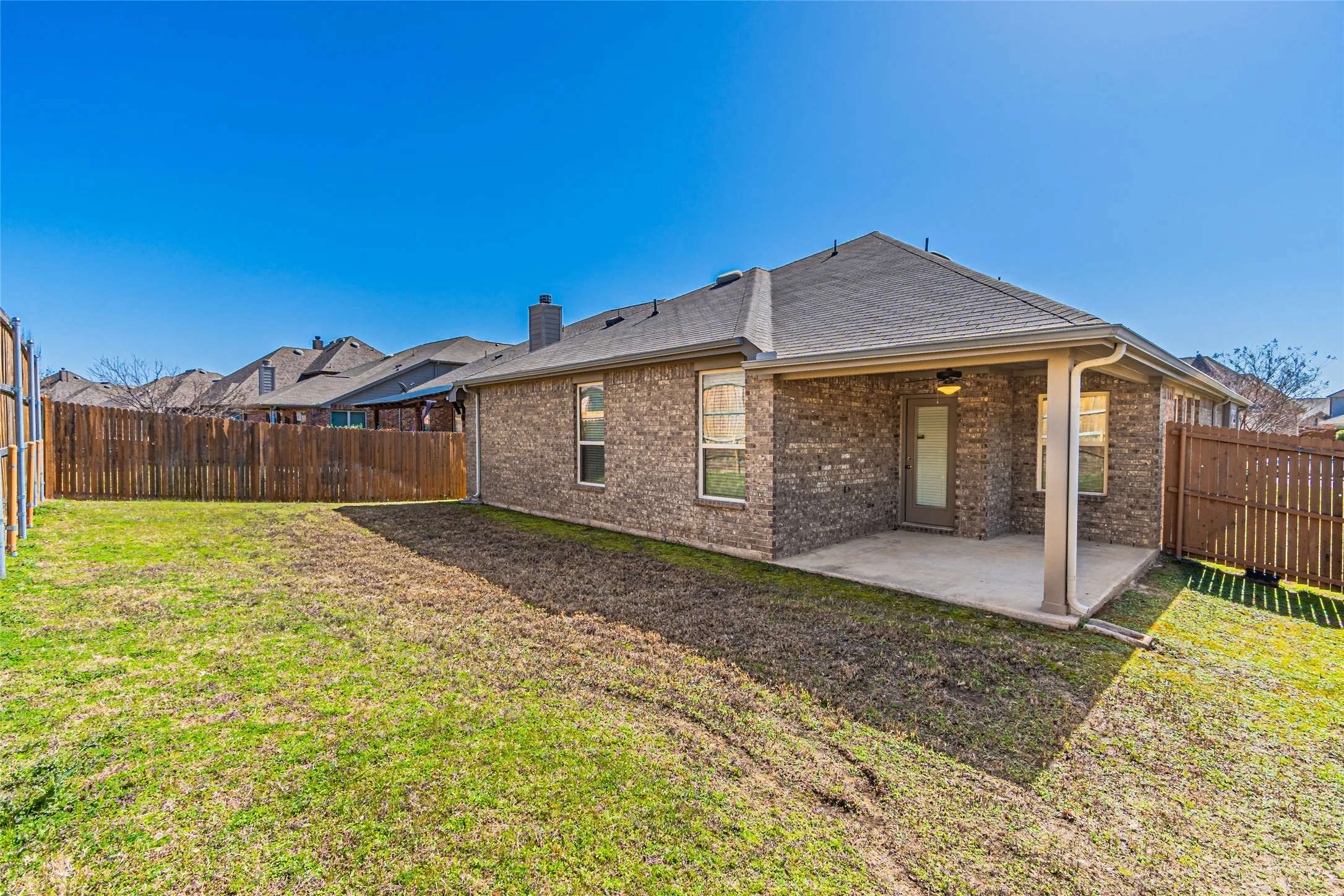 Rear exterior featuring a brick facade, covered concrete patio, and a wood privacy fence