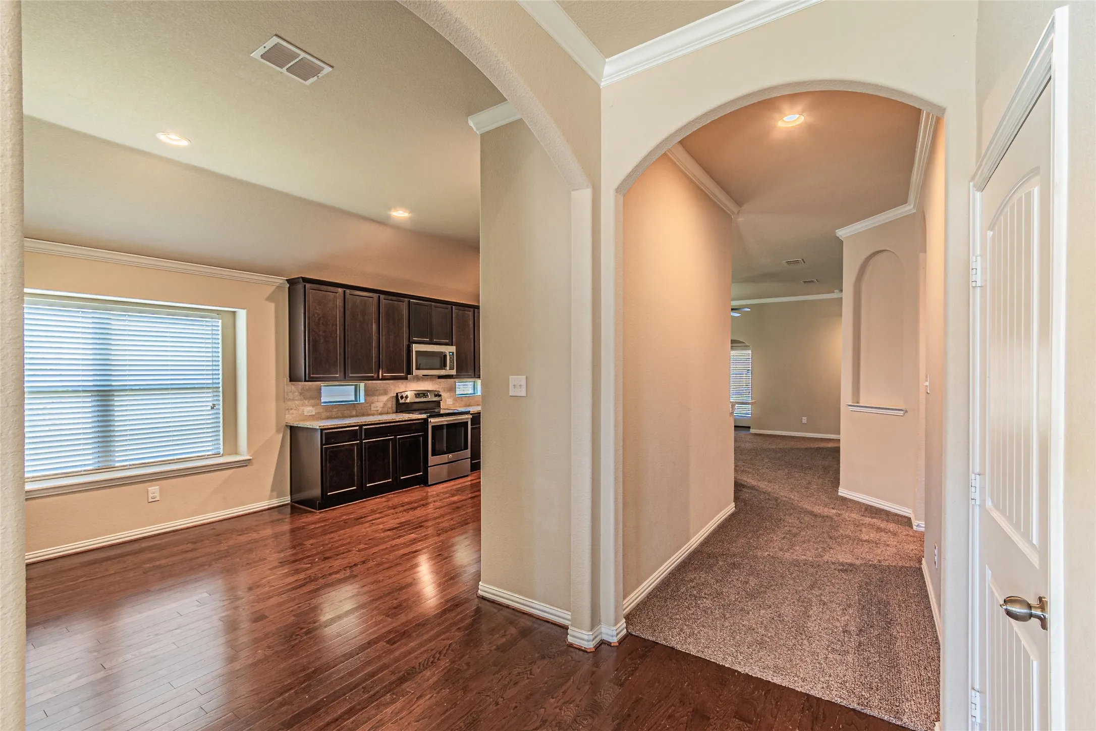 Interior featuring arched architectural detailing, dark-toned cabinetry, wood-finish flooring, recessed lighting, and crown molding