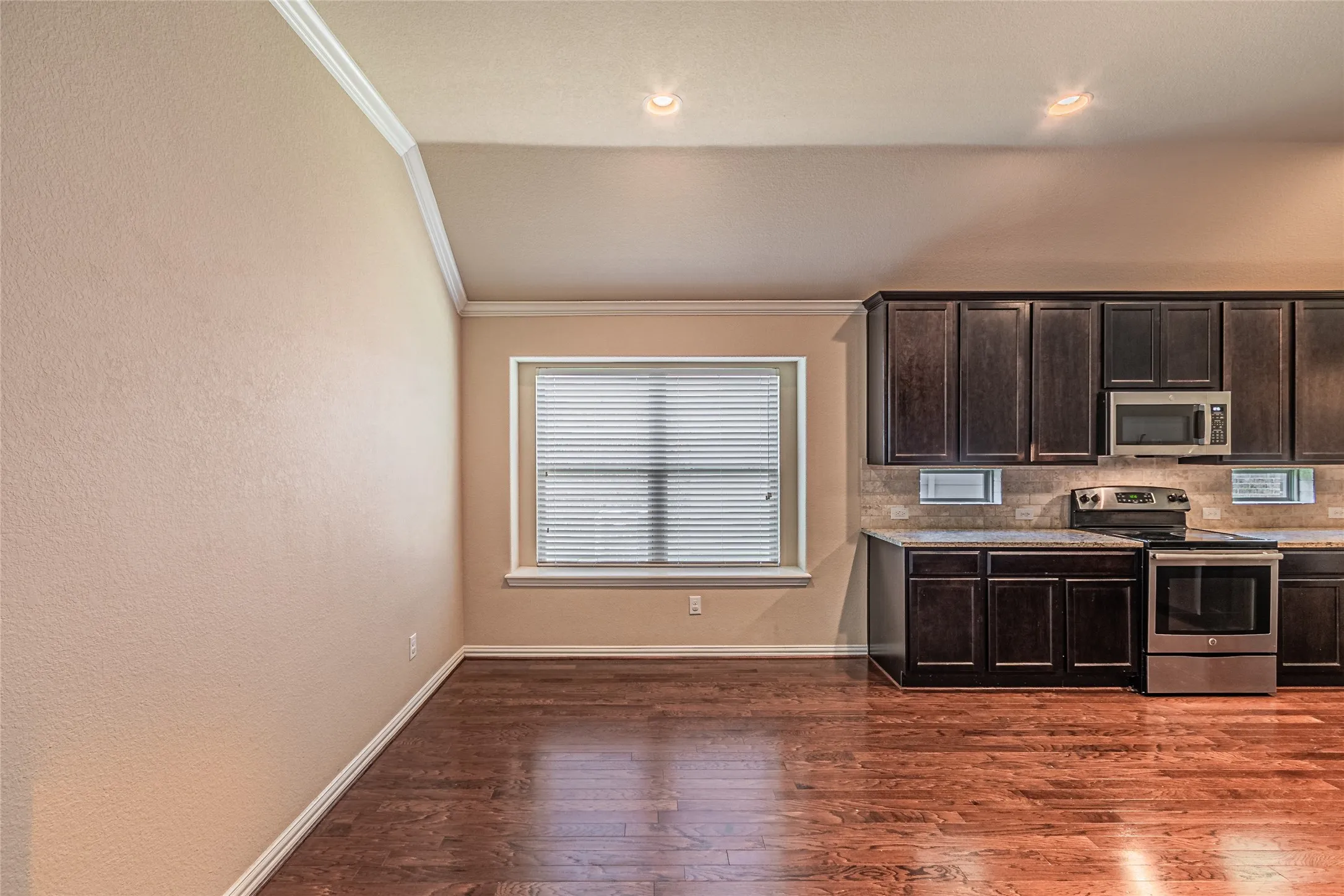 Kitchen featuring wood-finish flooring, dark-toned cabinetry, stainless steel appliances, and a vaulted ceiling with crown molding