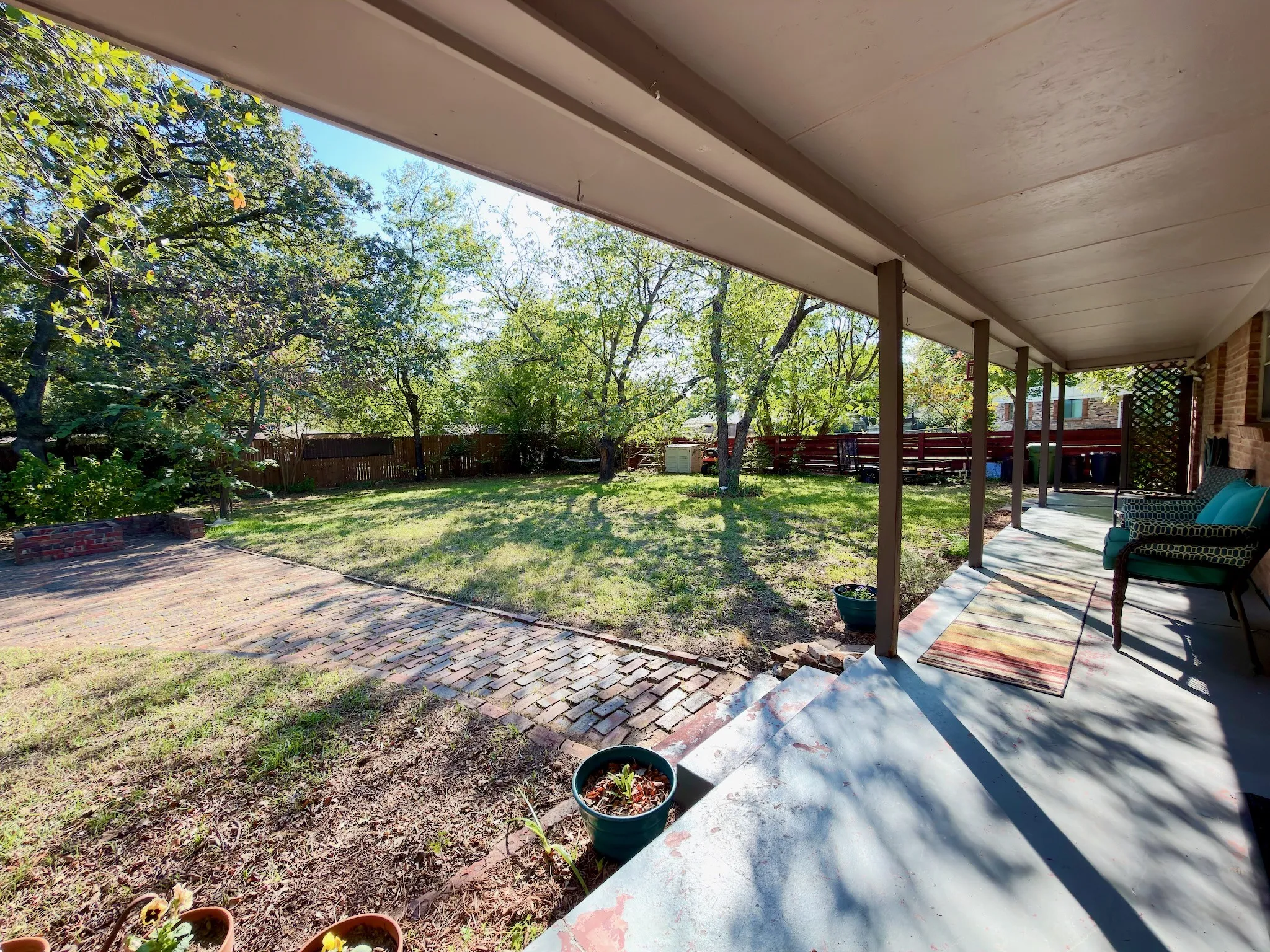 Covered patio featuring a solid ceiling, brick paver hardscaping, mature trees, and a perimeter wood-slat fence