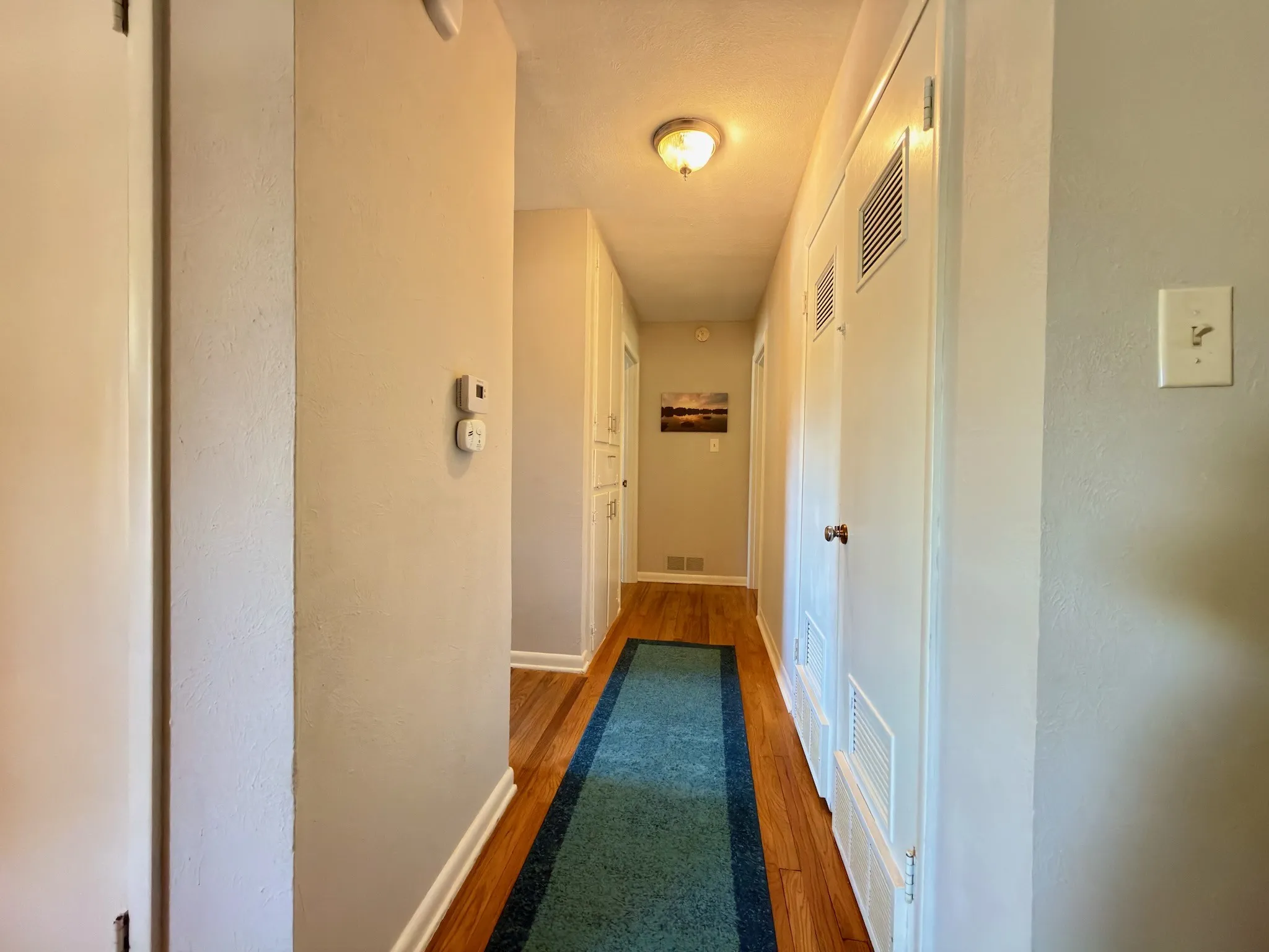 Hallway featuring wood-finish flooring, built-in cabinetry, flush-mount ceiling lighting, and multiple interior doors with louvered panels HVAC & water heater  closet