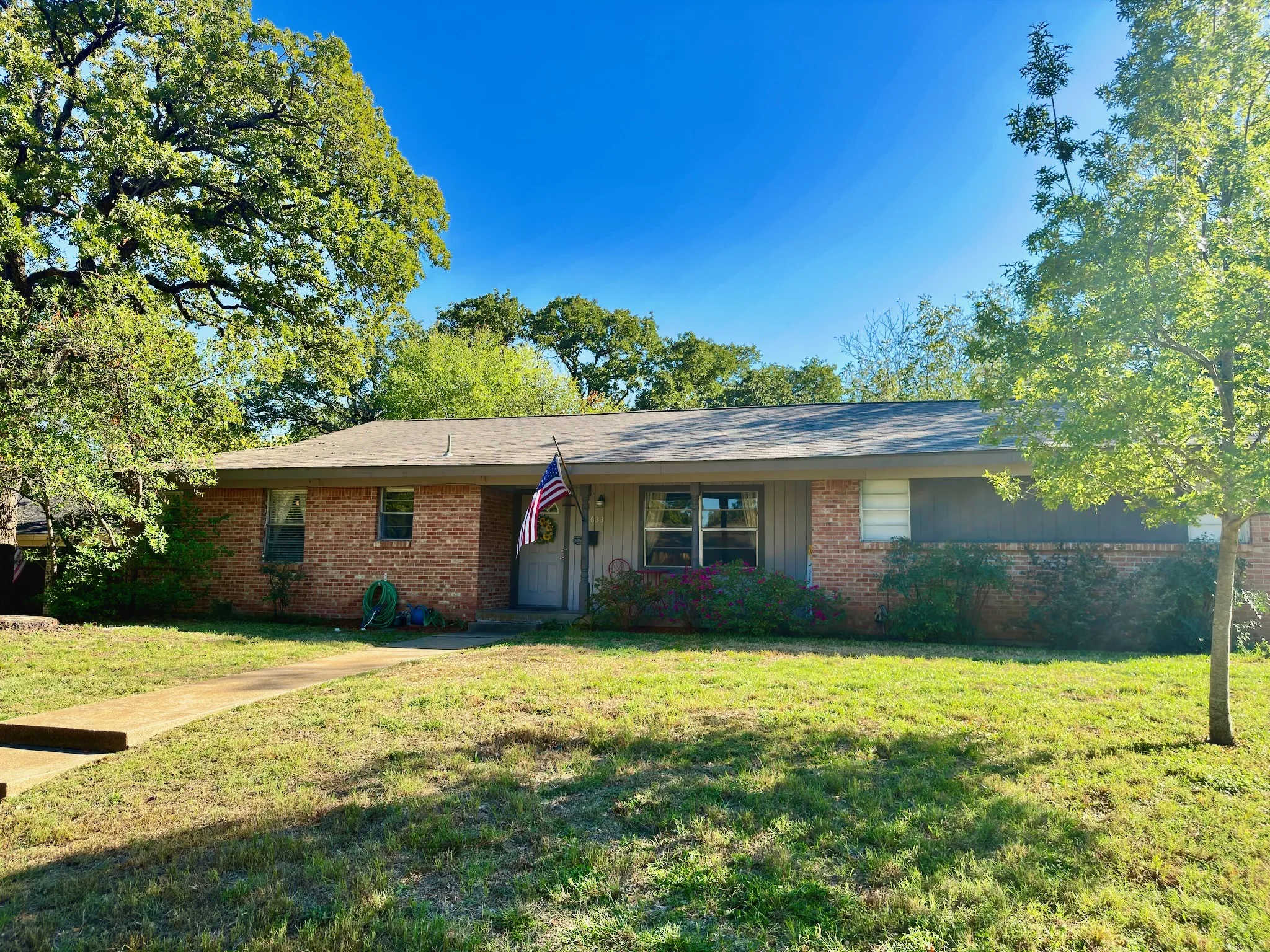 1616sf 3/2/2 Single-story exterior featuring a brick facade, vertical wood-panel siding, mature shade trees, and a concrete walkway