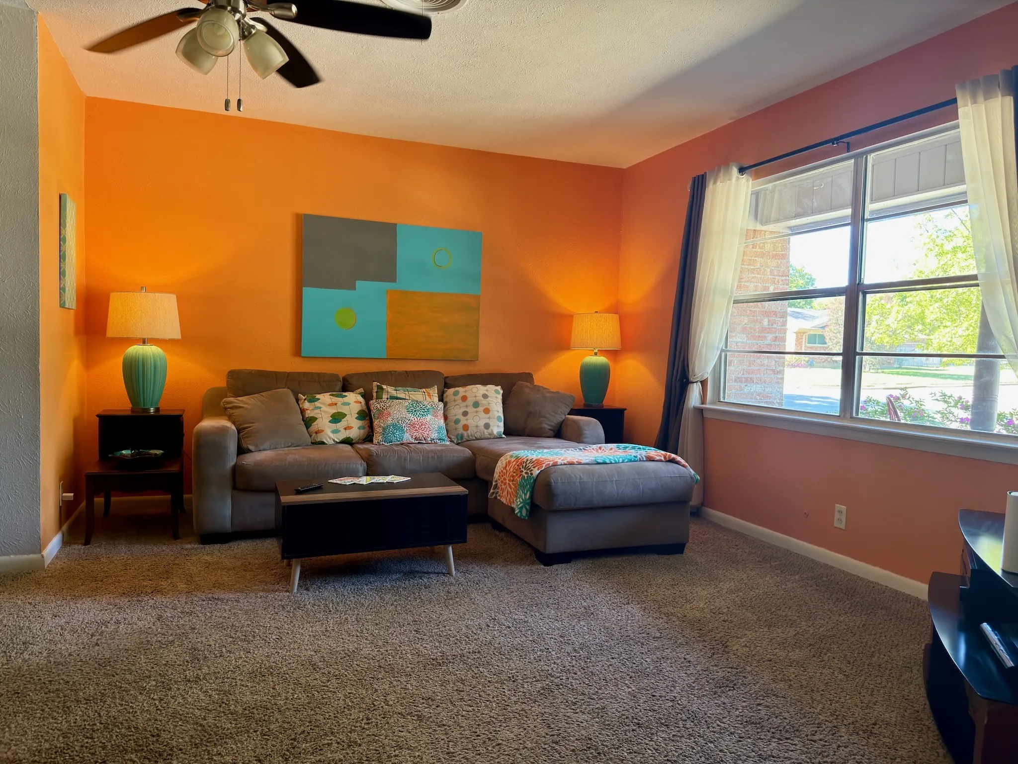 Living area featuring wall-to-wall carpeting, a multi-pane window, and a ceiling fan with integrated lighting