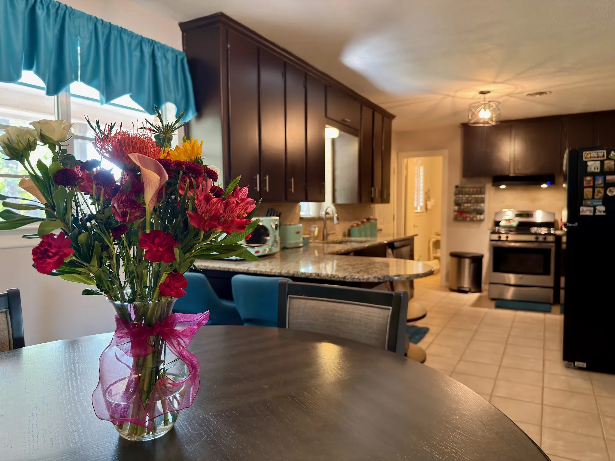 Dining to Kitchen view featuring dark-finish cabinetry, stone-surface countertops, tile flooring, stainless steel appliances, and a peninsula-style counter