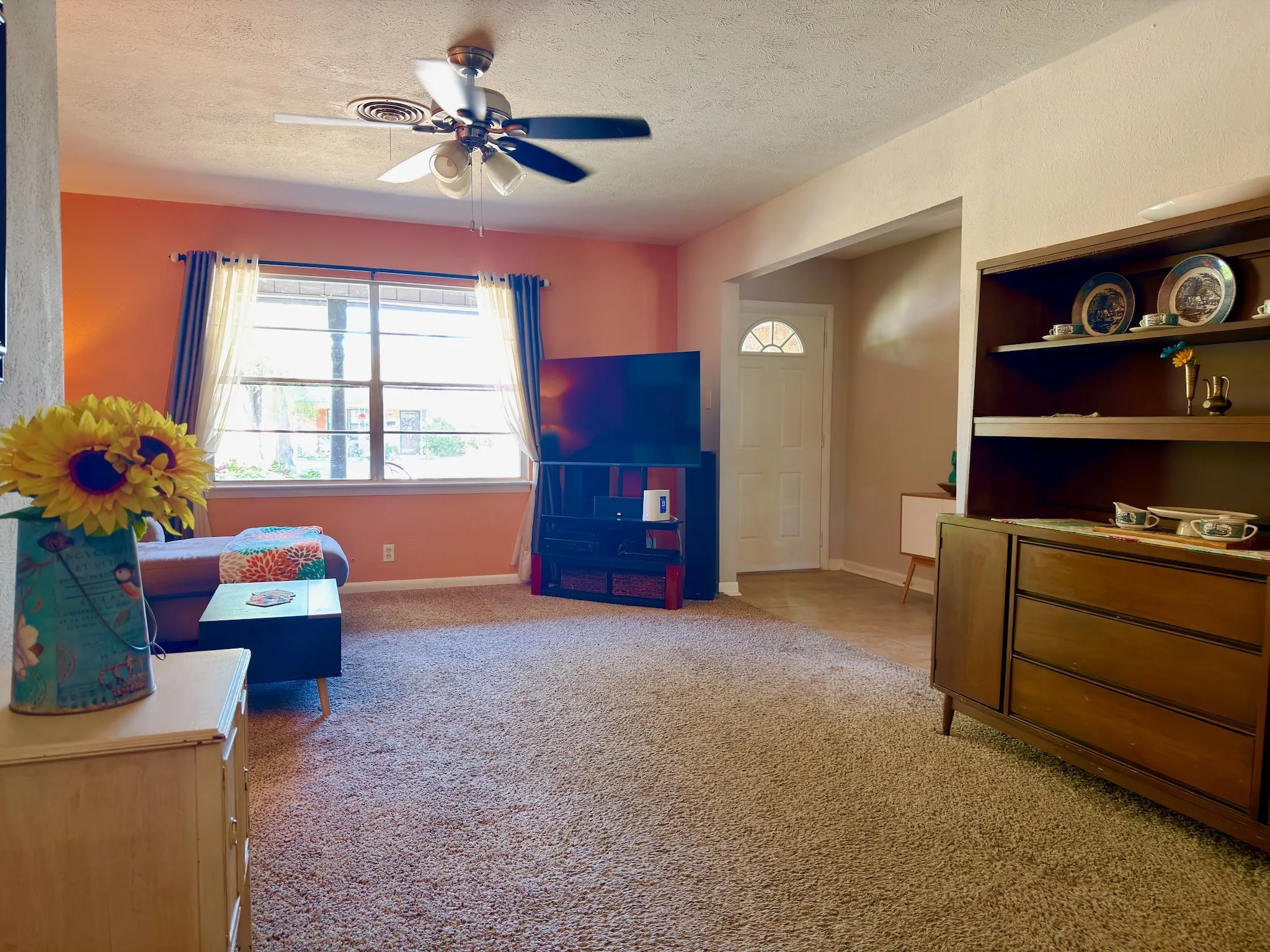 Living area featuring wall-to-wall carpeting, a multi-pane window, and a ceiling fan with integrated lighting