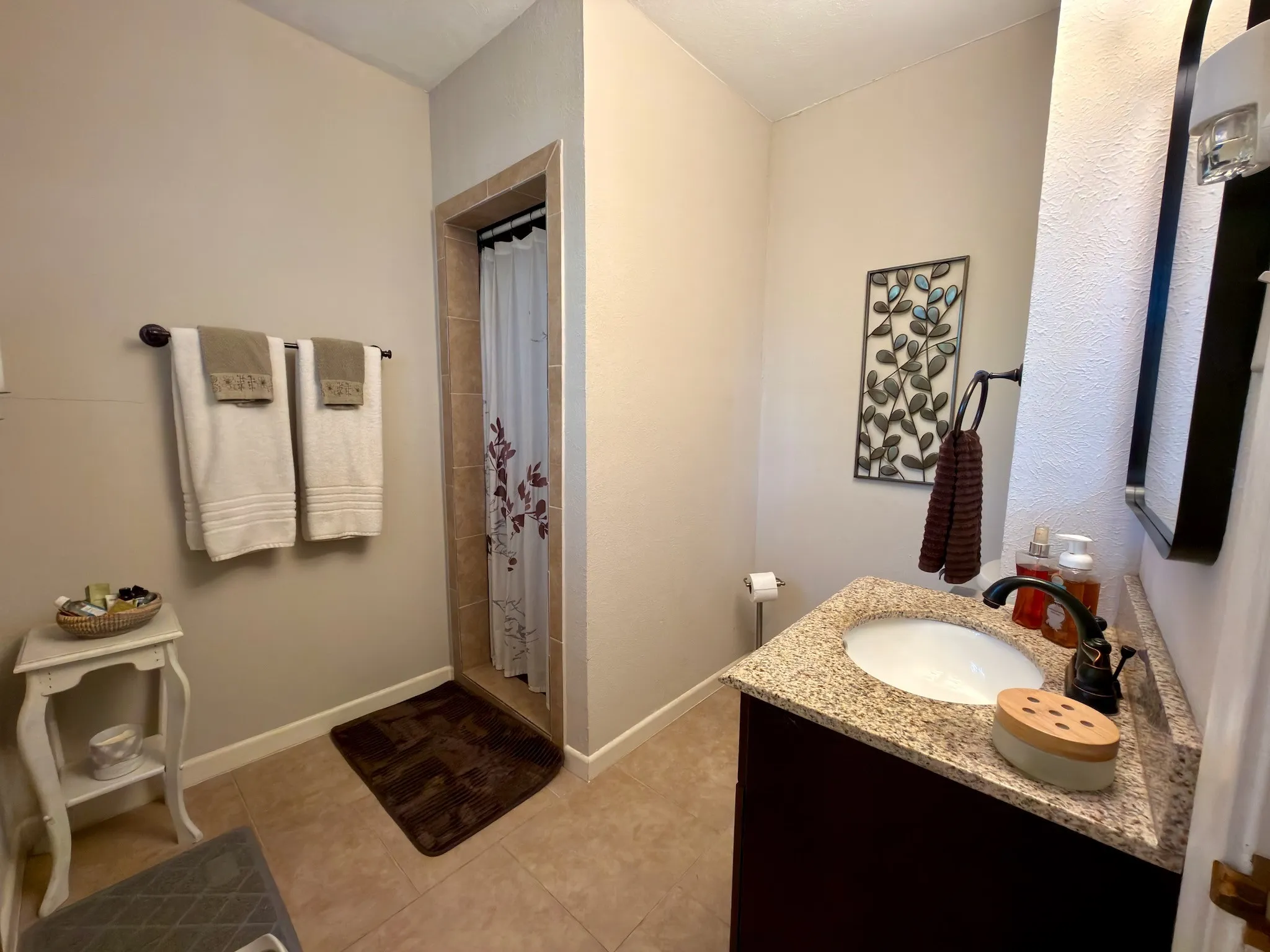 Bathroom featuring a dark wood-finish vanity, stone-patterned countertop, integrated undermount sink, oil-rubbed bronze hardware, and tile flooring