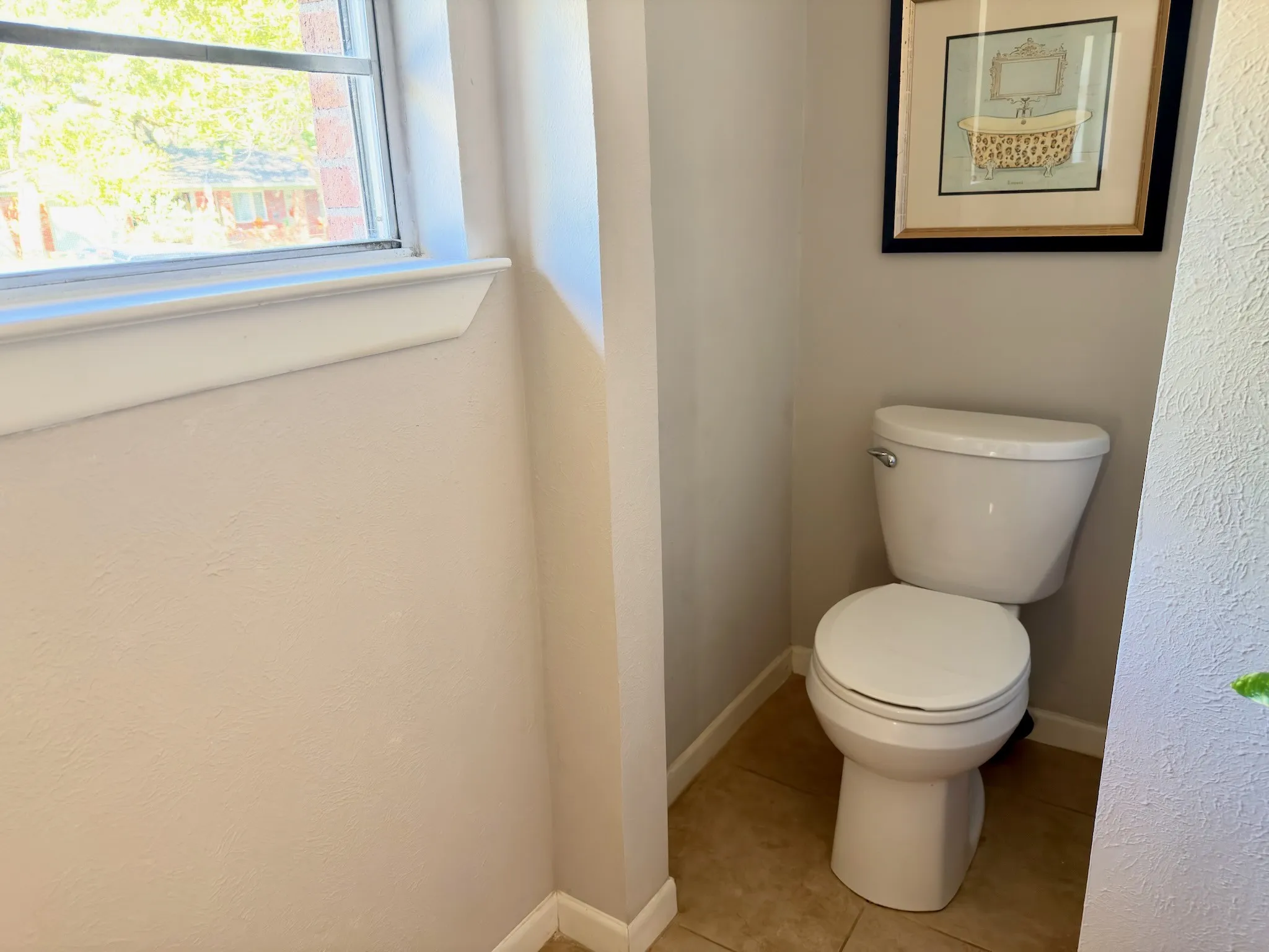 Porcelain toilet with a neutral-toned tile floor and a single-hung window featuring a deep sill