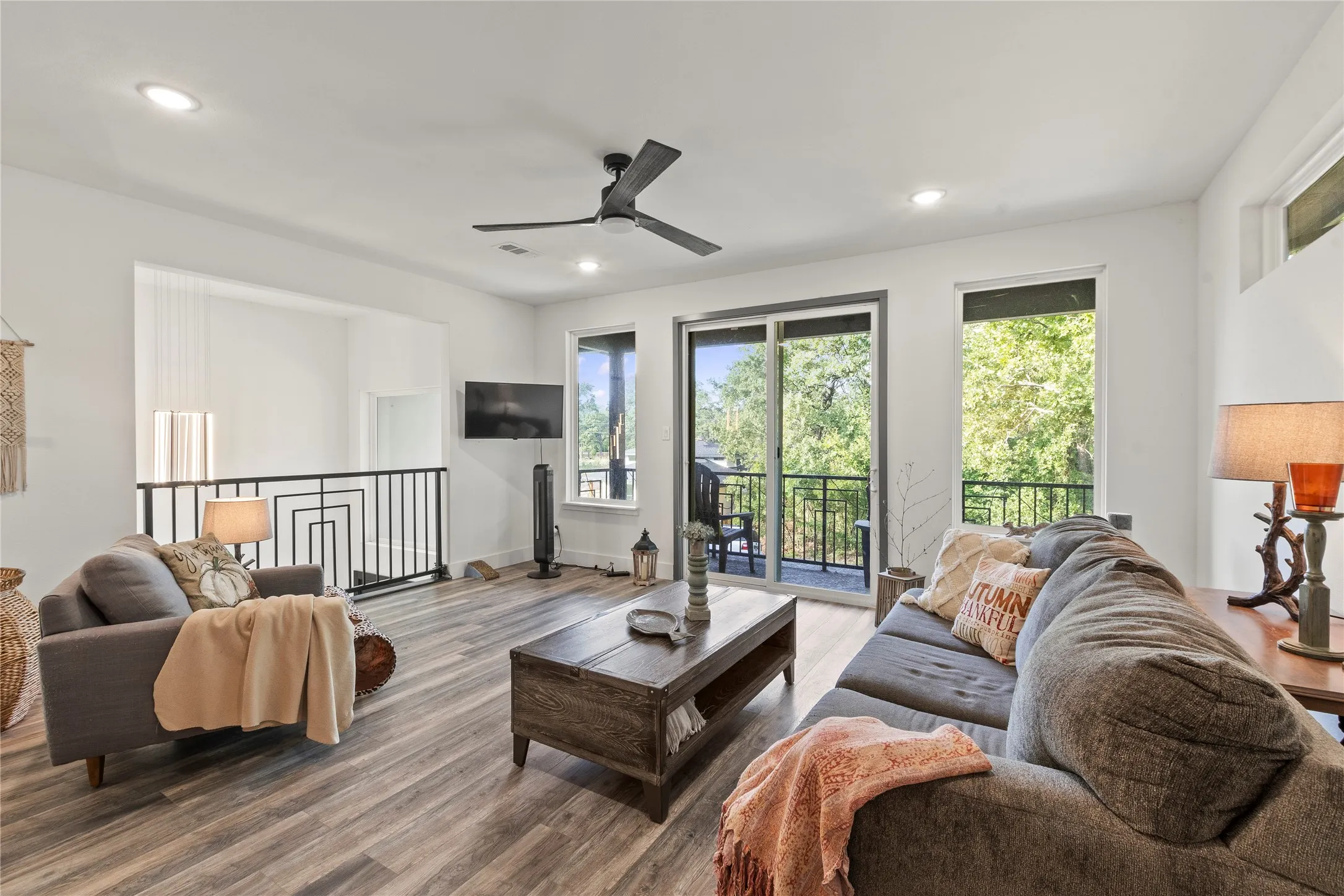 Living area featuring wood-finish flooring, recessed lighting, a modern ceiling fan, sliding glass doors to a balcony, and decorative metal railings