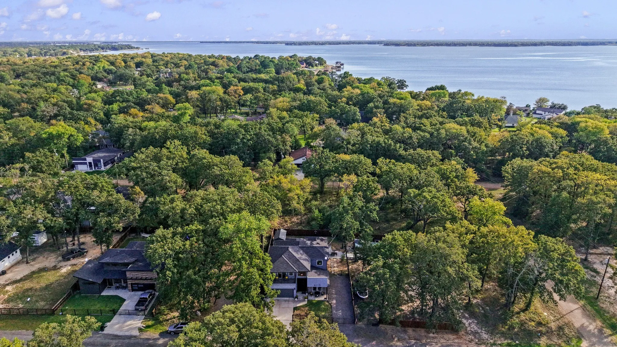 Aerial perspective featuring a multi-story residence with a pitched roof, concrete driveway, and established canopy of mature trees