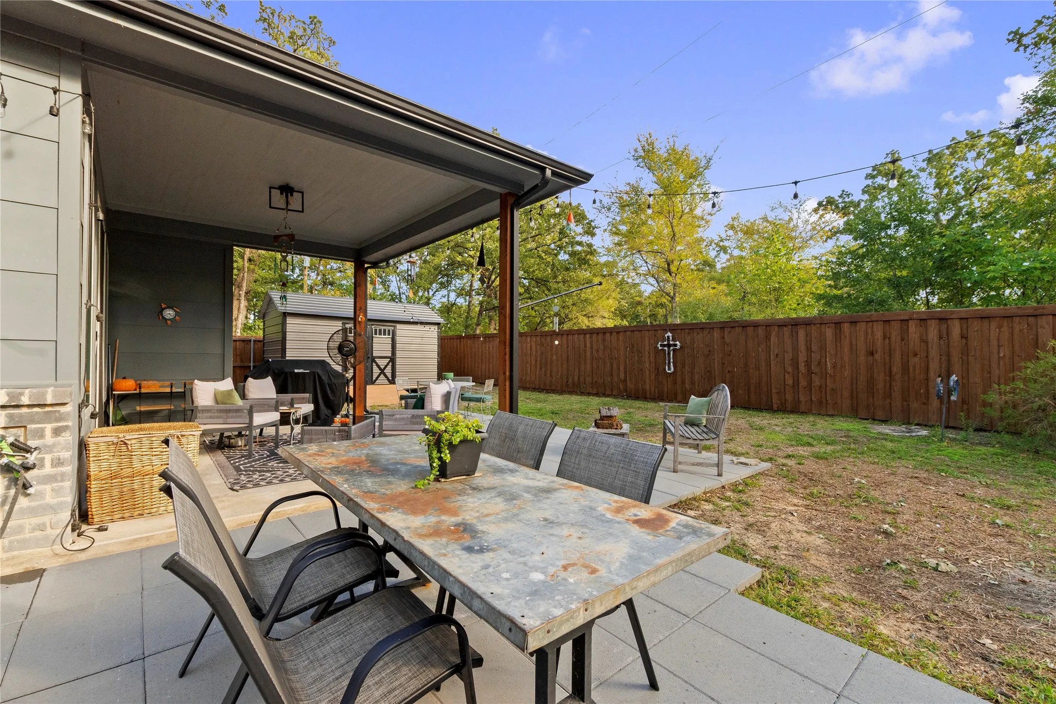 Covered rear patio with large-format concrete pavers, wood-slat privacy fencing, and exterior string lighting