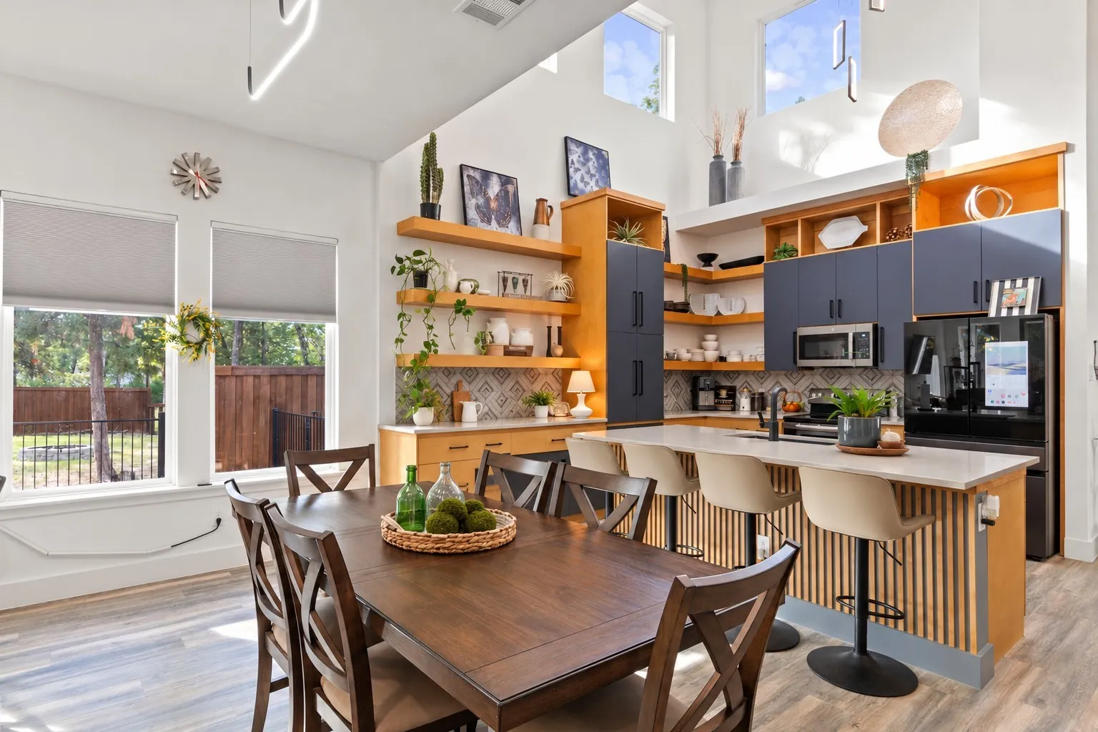 High-ceiling kitchen featuring a dual-toned cabinetry finish, wood-finish flooring, floating wood shelving, a central island with a slatted wood base, and geometric tile backsplash