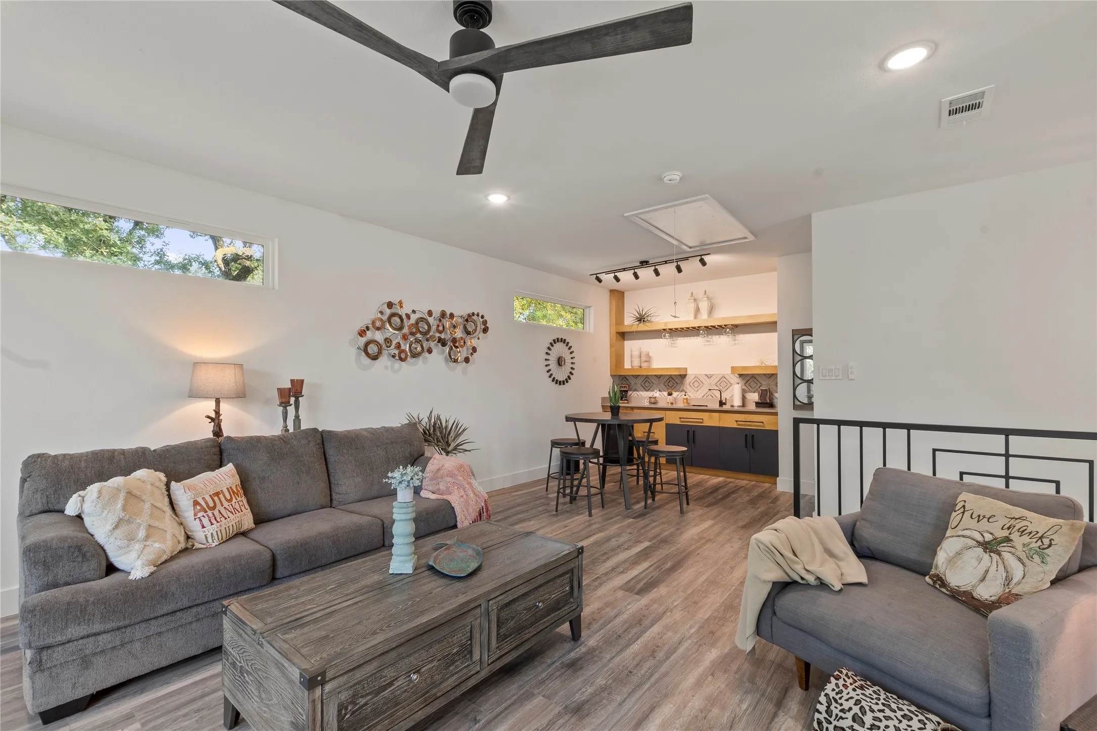 Wood-finish flooring, matte black three-blade ceiling fan, transom windows, built-in wet bar with natural wood shelving, and patterned tile backsplash