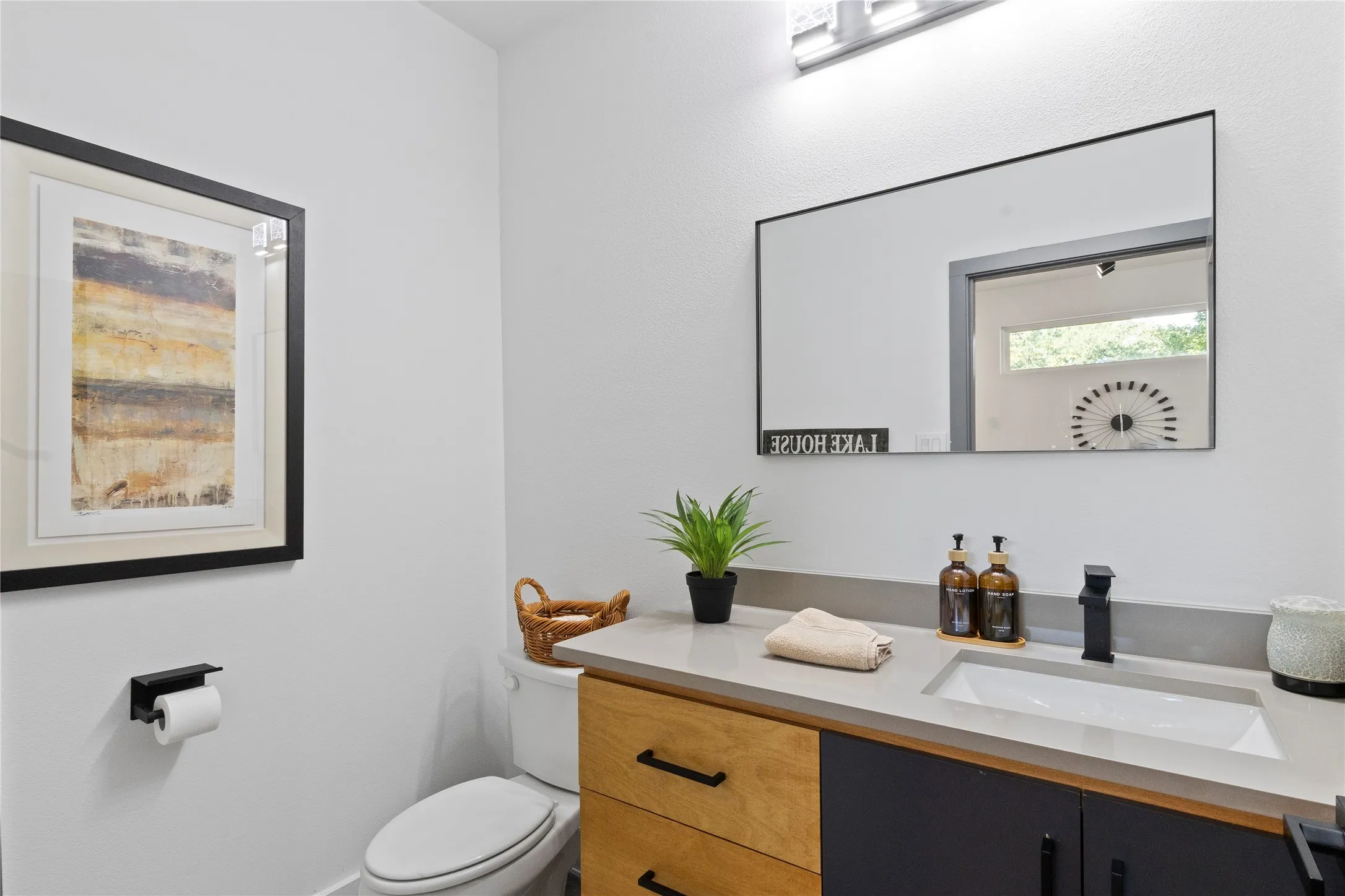 Vanity featuring dual-tone cabinetry, stone-composite countertop with integrated sink, matte black faucet, and rectangular wall-mounted mirror