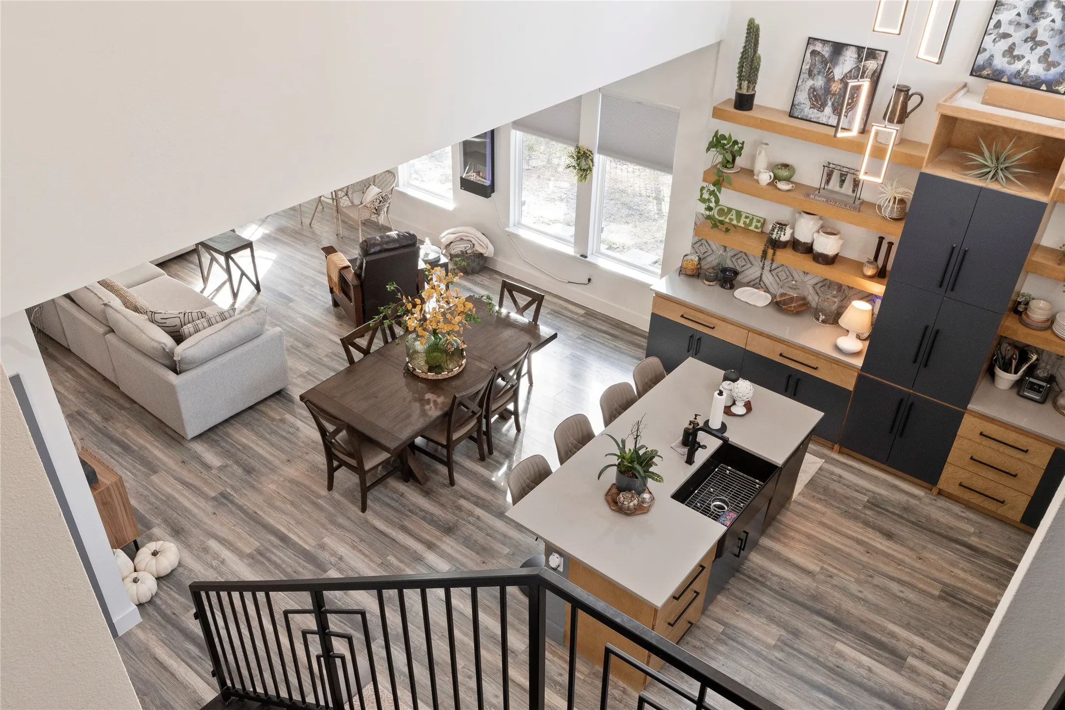 Open-concept interior featuring two-story ceilings, wood-finish flooring, and a kitchen island with a rectangular basin sink and matte black hardware