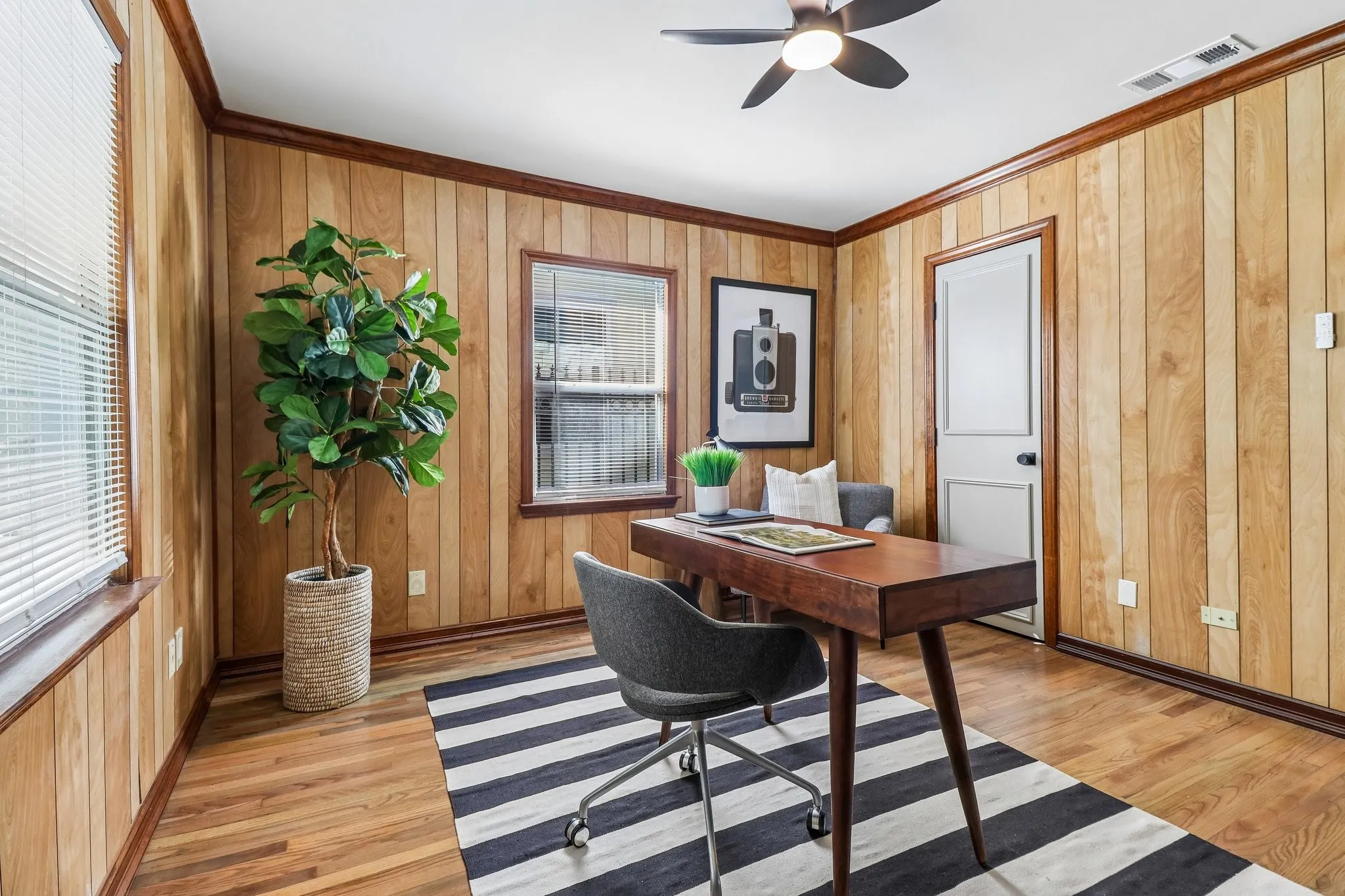 Wood-paneled walls with coordinating wood-finish flooring, ceiling fan with integrated lighting, and a white paneled door