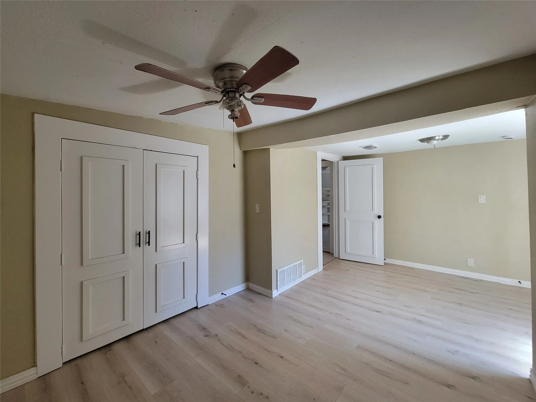 Wood-finish flooring, double-panel closet doors with matte black hardware, and a ceiling fan with integrated lighting