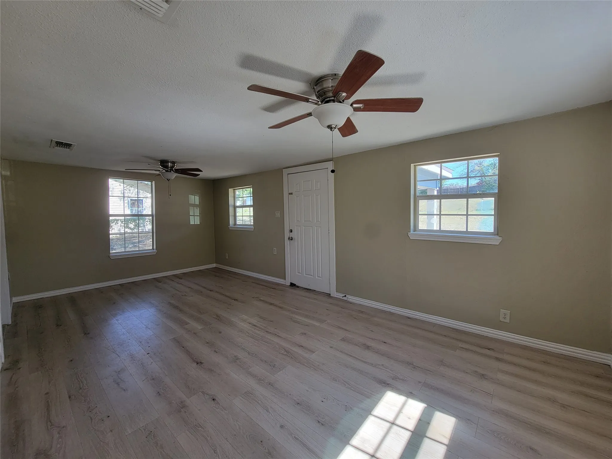 Interior space featuring wood-finish flooring, two ceiling fans with integrated lighting, multiple windows, and a panel-style door