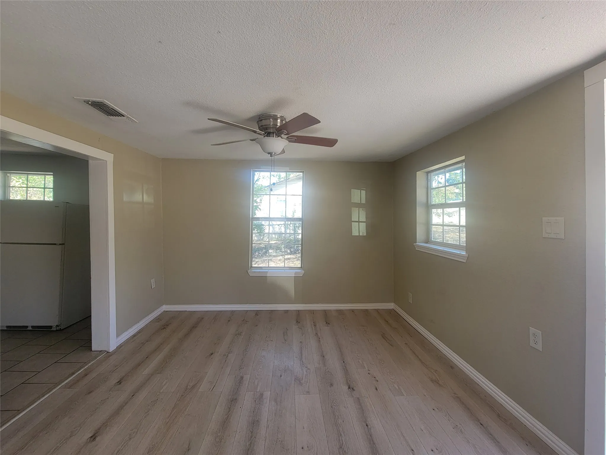 Neutral-toned interior space featuring light-toned wood-finish flooring, dual windows, and a ceiling-mounted fan with light fixture
