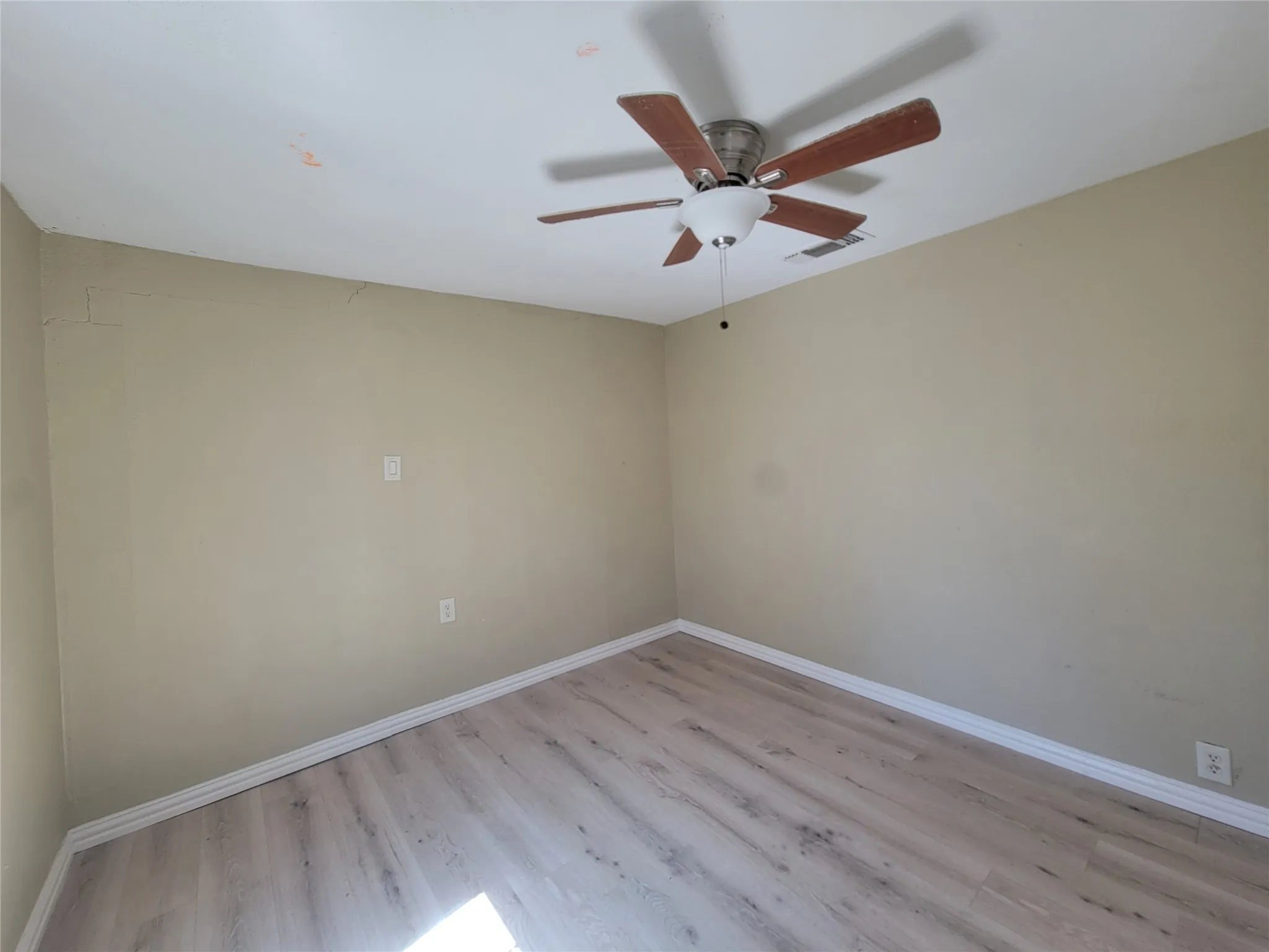 Interior space featuring wood-finish flooring, neutral wall tones, and a ceiling-mounted light fixture with a five-blade fan