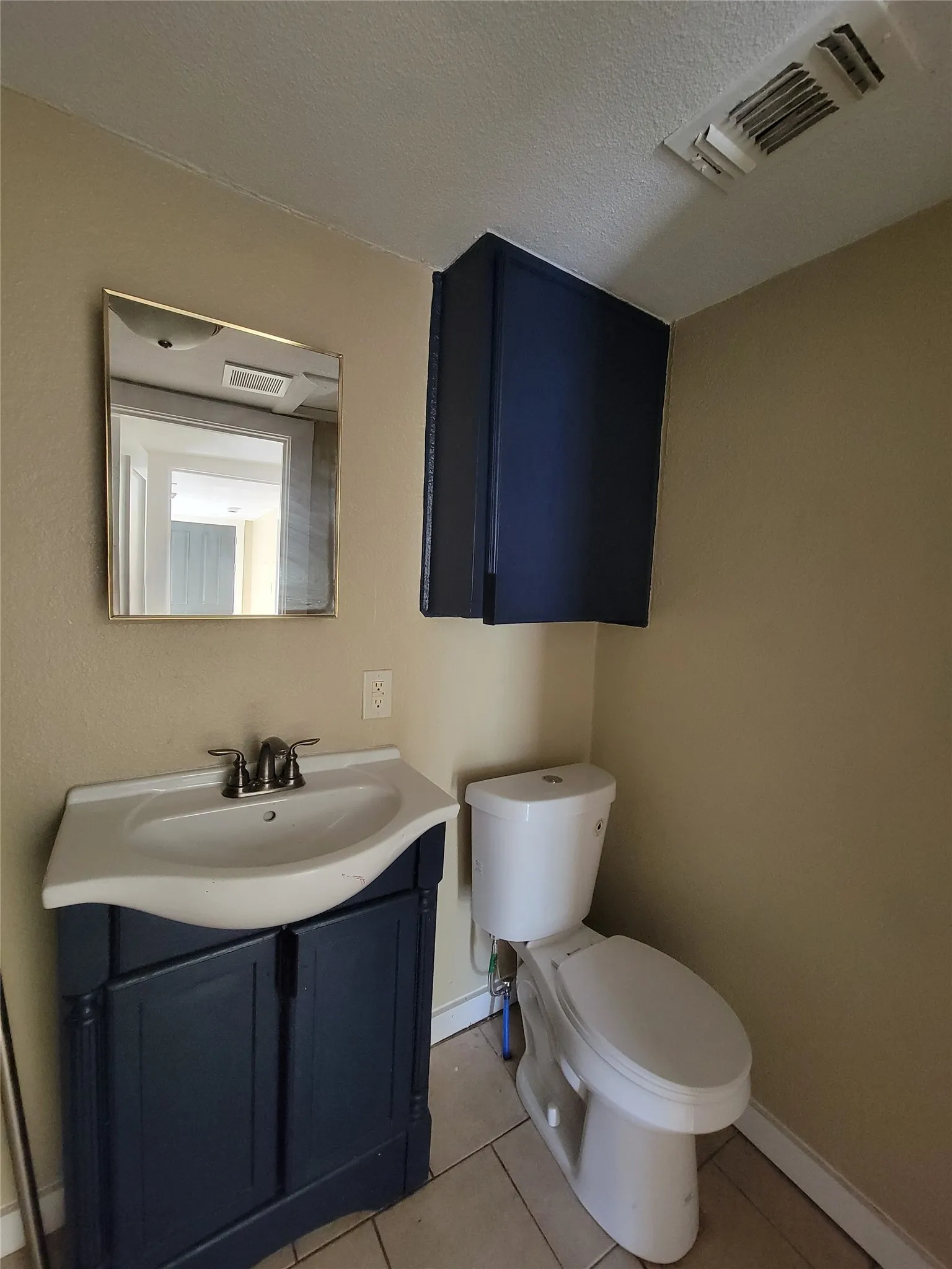 Bathroom featuring a navy blue vanity cabinet, integrated sink with a dual-handle faucet, wall-mounted storage cabinet, and tile flooring