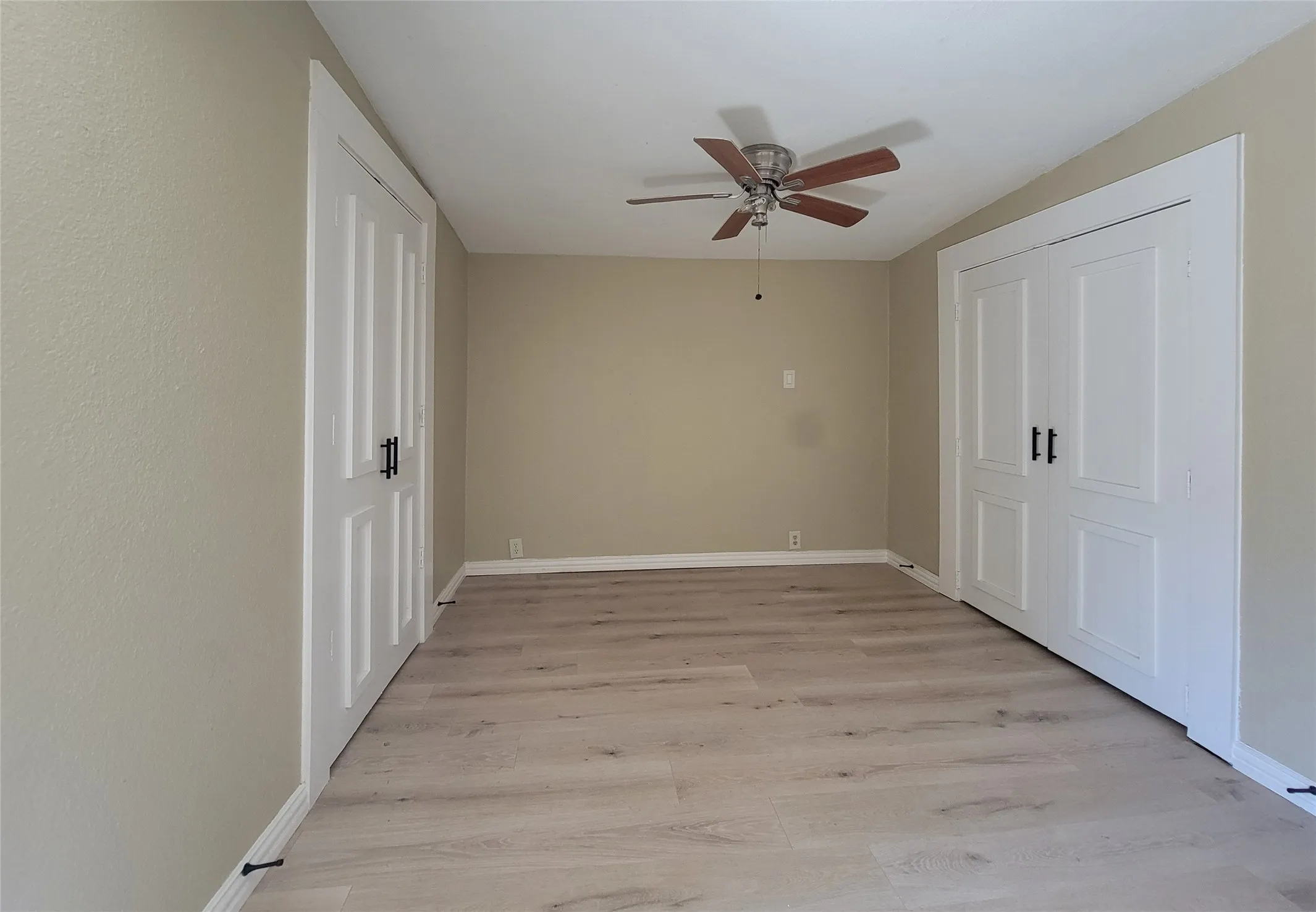 Interior room featuring wood-finish flooring, two sets of double-panel doors with matte black hardware, and a ceiling-mounted fan with wooden blades