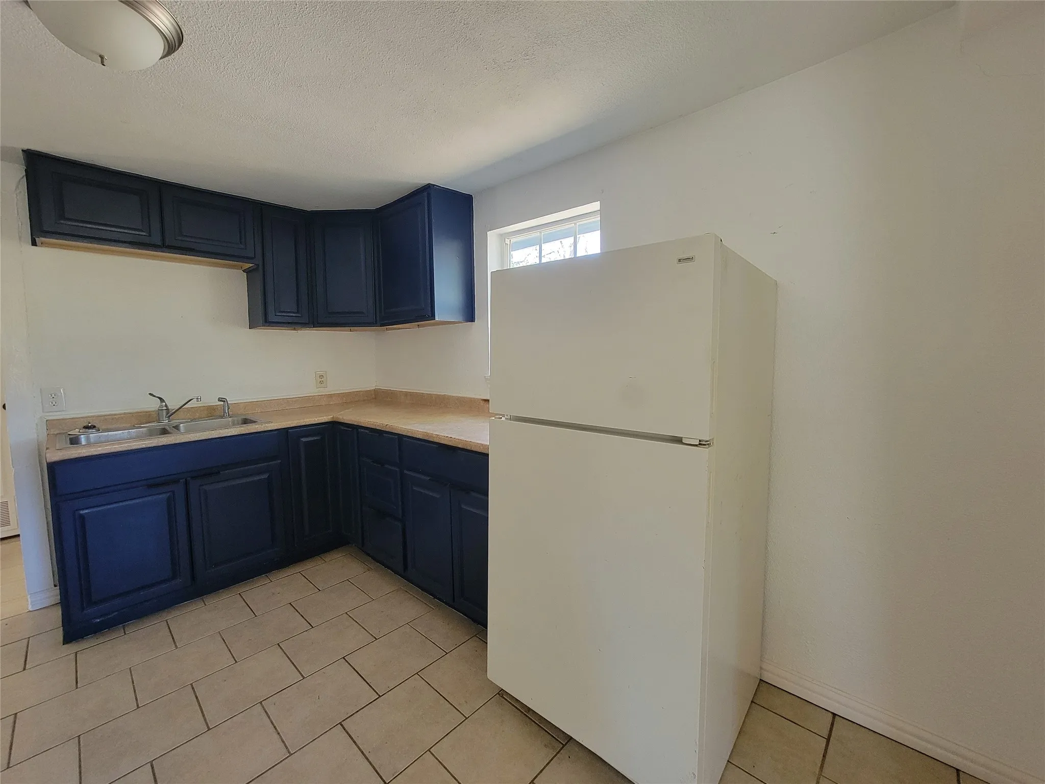 Kitchen featuring navy cabinetry, solid surface countertops, dual-basin stainless steel sink, large refrigerator, and tiled flooring