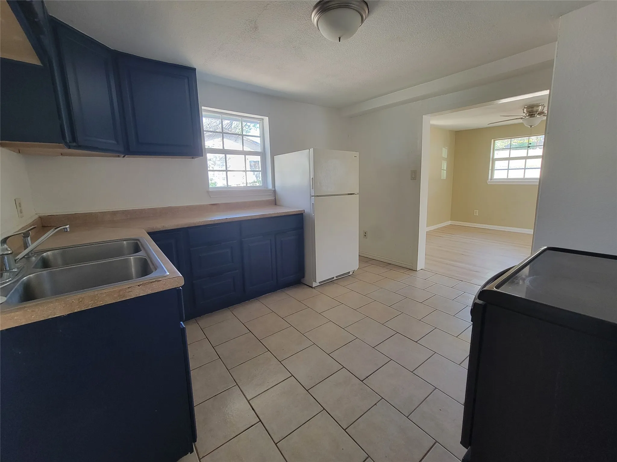 Kitchen featuring dark cabinetry, ceramic tile flooring, double-basin stainless steel sink, and windows with paneled grids