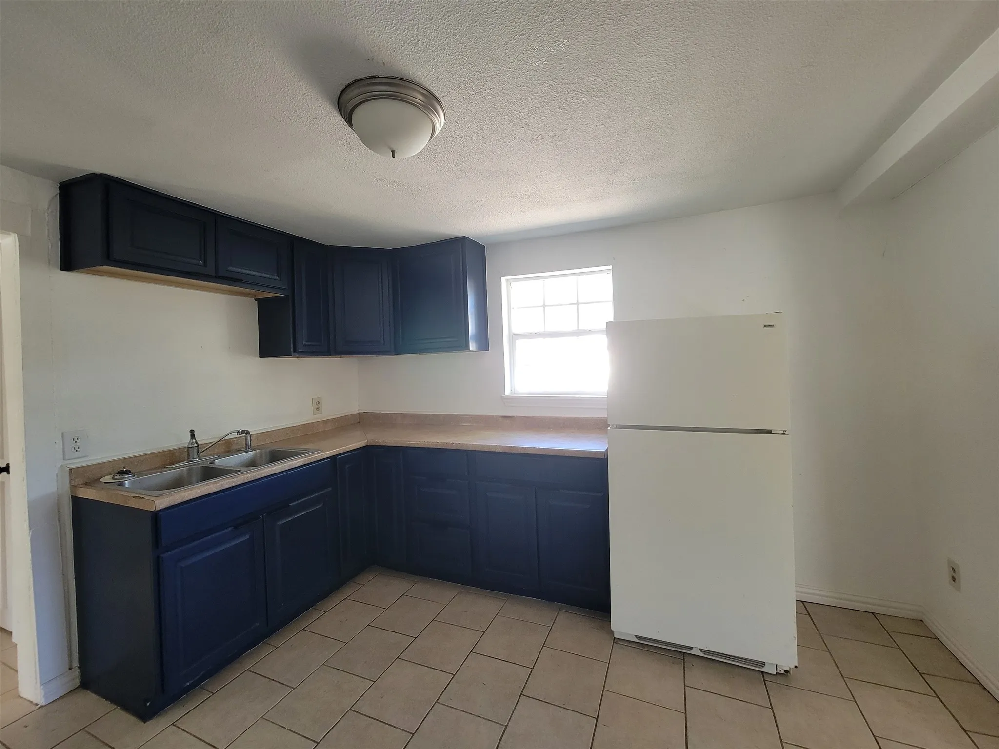 Kitchen featuring dark blue cabinetry, laminate countertops, a dual-basin stainless steel sink, ceramic tile flooring, and a window