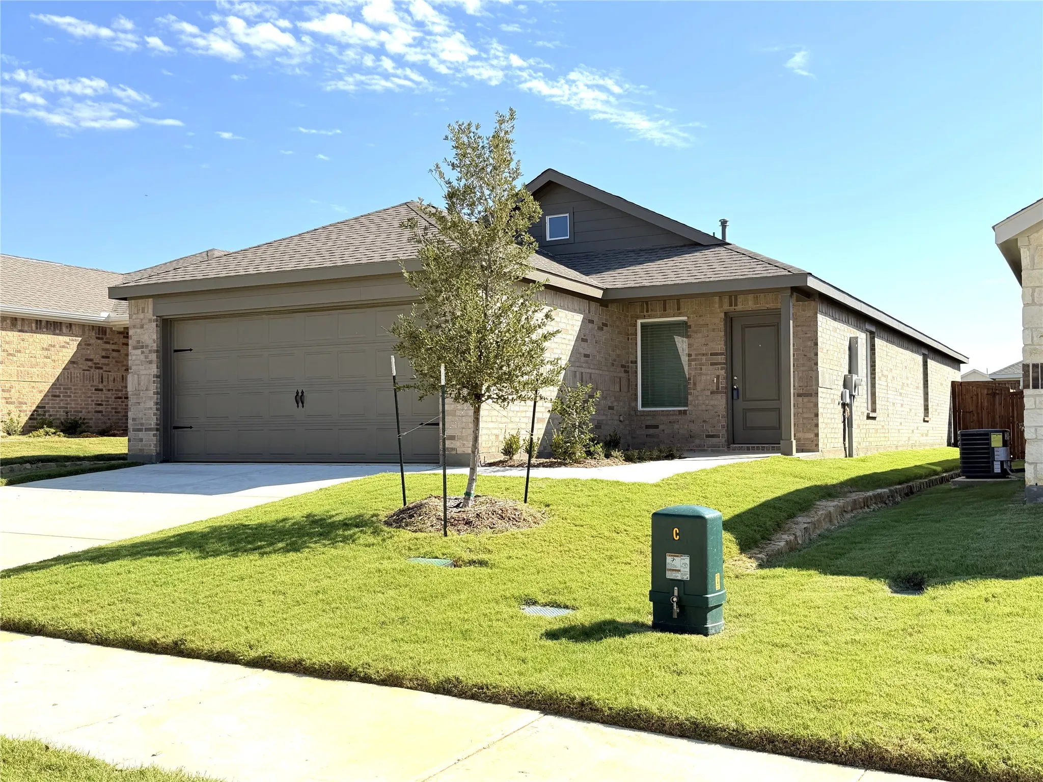 Single-story exterior featuring a brick facade, gabled roofline, concrete driveway, and an attached two-car garage
