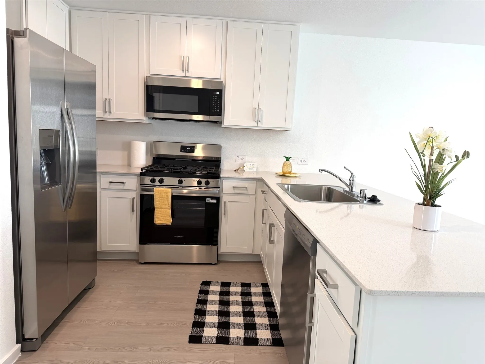 Kitchen featuring white cabinetry, stainless steel appliances, quartz countertops, a stainless-steel sink with a pull-down faucet, and wood-finish flooring