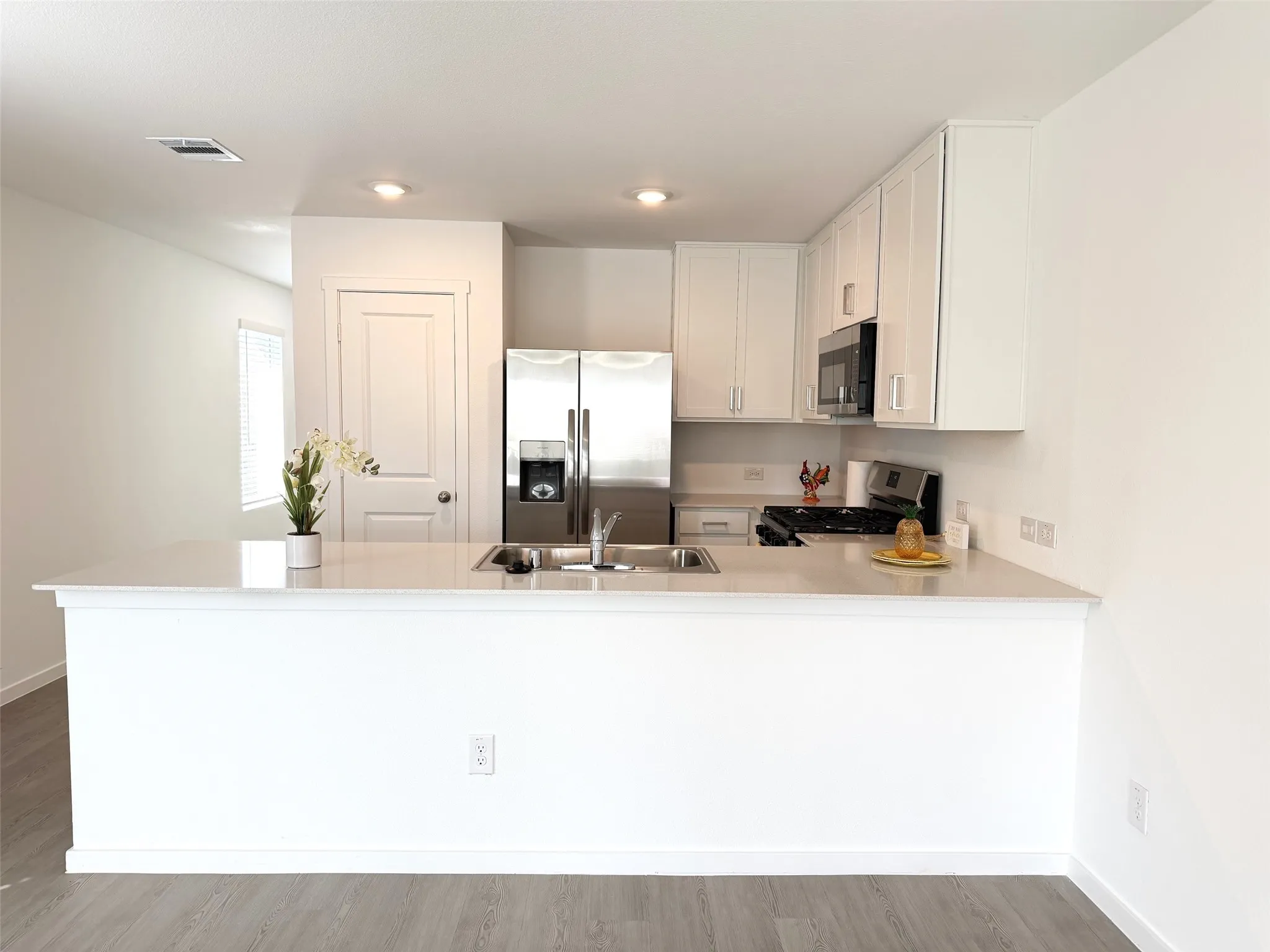 Kitchen featuring a central island with a quartz countertop, white cabinetry, stainless steel appliances, and wood-finish flooring