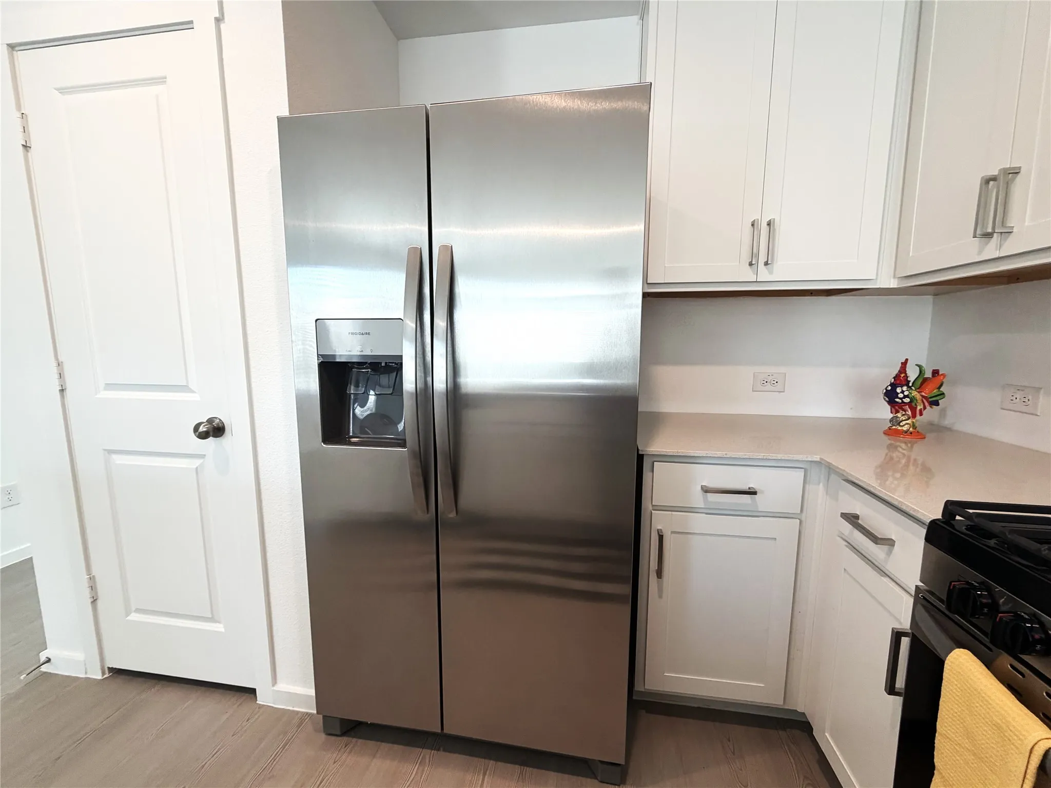 Stainless steel side-by-side refrigerator, white shaker-style cabinetry with satin nickel hardware, light-quartz countertops, and wood-finish flooring