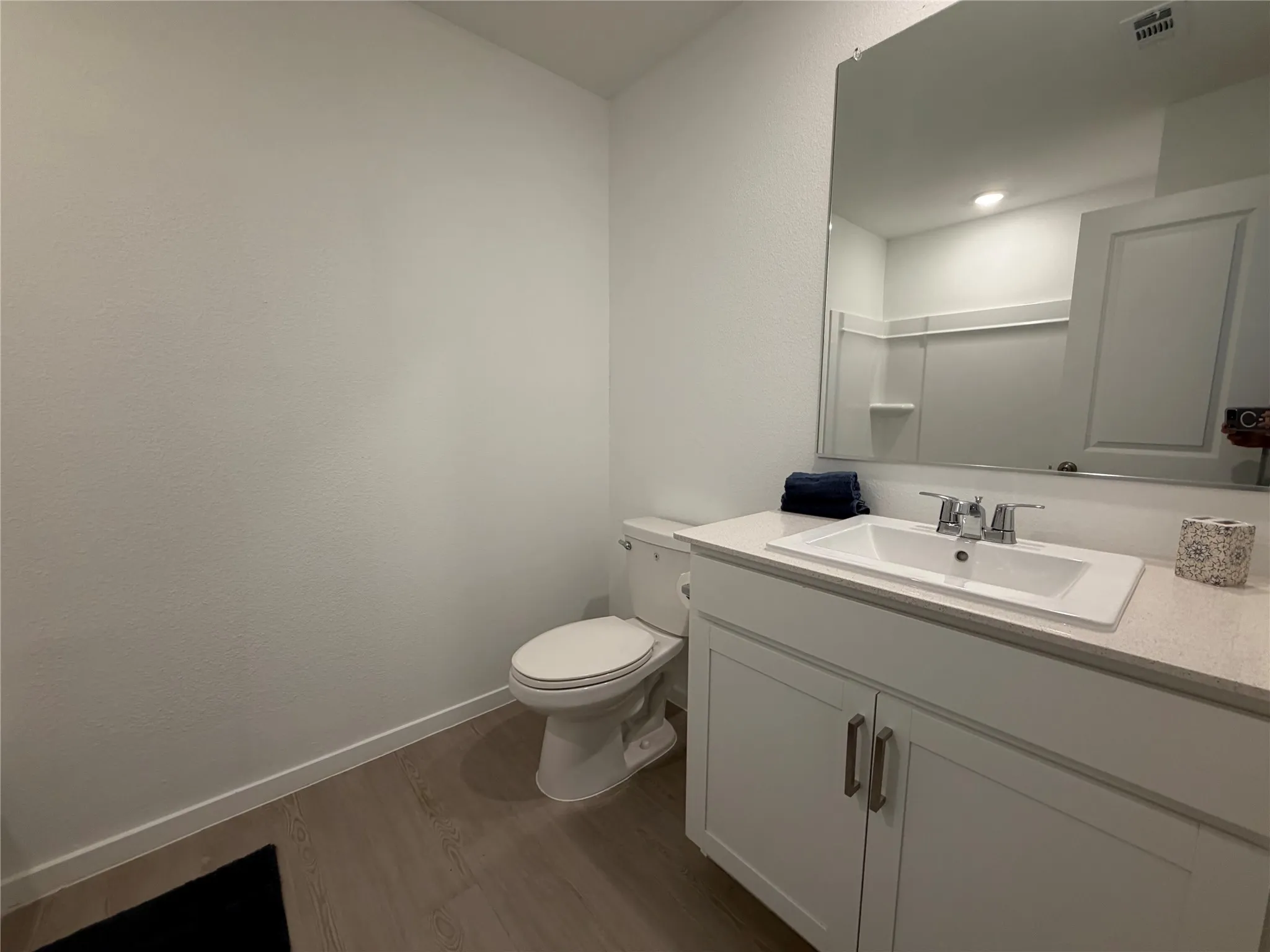 Bathroom featuring a white vanity cabinet with a quartz countertop, integrated rectangular sink, chrome dual-handle faucet, large wall-mounted mirror, and wood-finish flooring