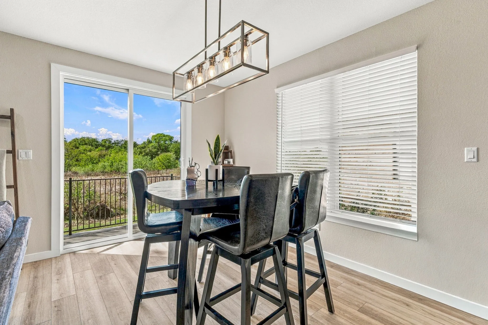 Dining space featuring wood-finish flooring, a contemporary rectangular pendant light fixture, a wide sliding glass door, and a multi-pane window with horizontal blinds