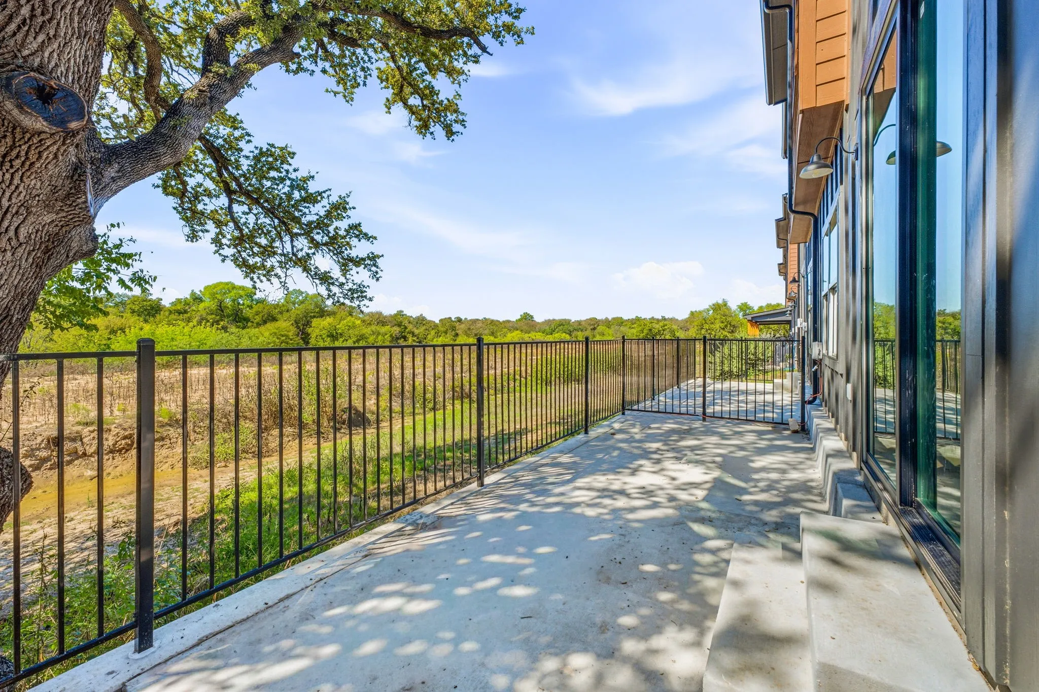 Concrete patio featuring metal perimeter fencing, exterior wall-mounted lighting, and oversized sliding glass doors