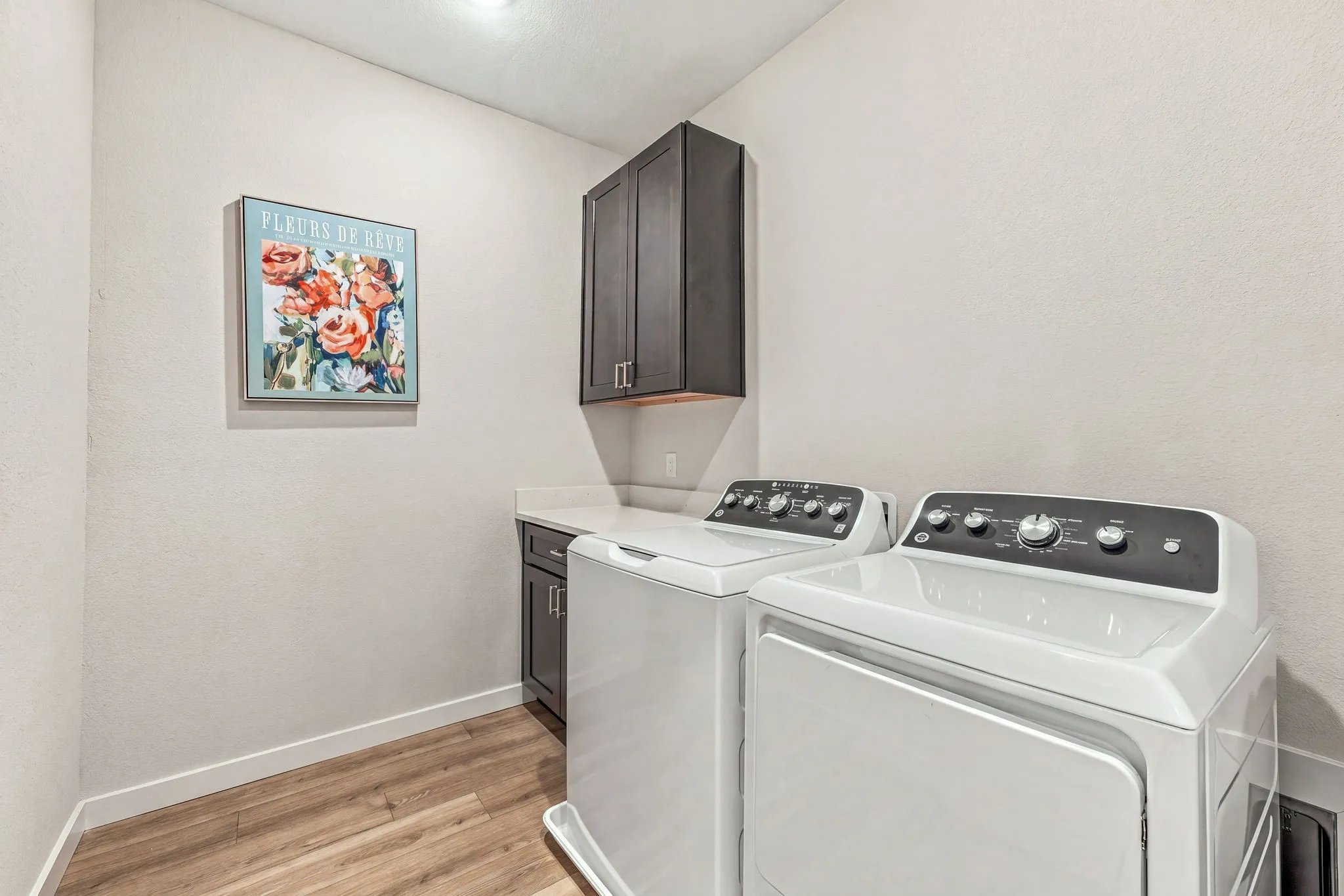 Utility room featuring wood-finish flooring, dark-toned upper and lower cabinetry, and a solid-surface countertop