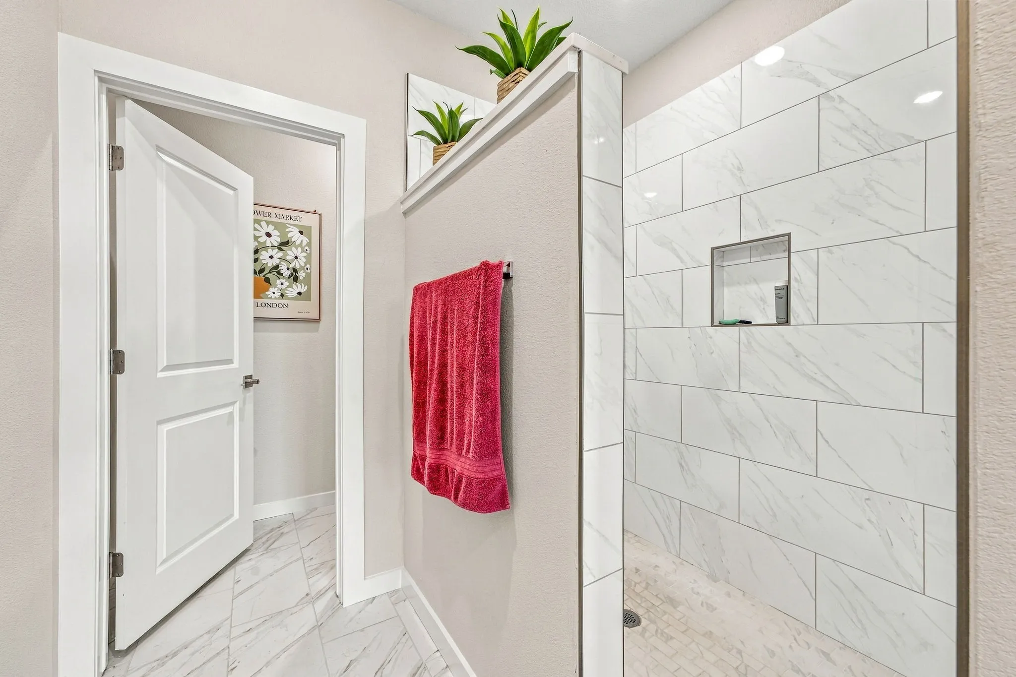 Walk-in shower featuring large-format rectified wall tile with veining, a built-in recessed wall niche, and stone-finish floor tile