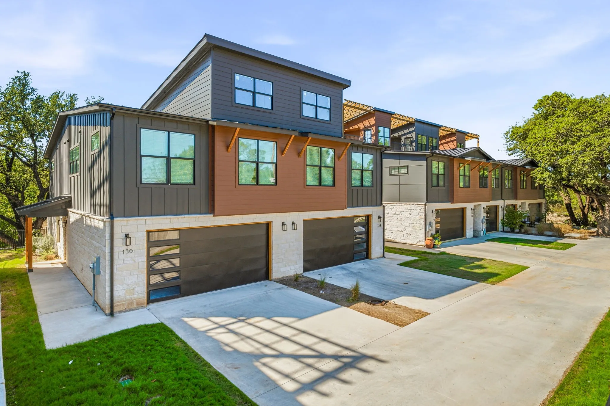 Multi-story exterior featuring a mix of stone veneer and vertical metal siding, contemporary oversized windows, modern horizontal-panel garage doors, and built-in exterior wall sconces
