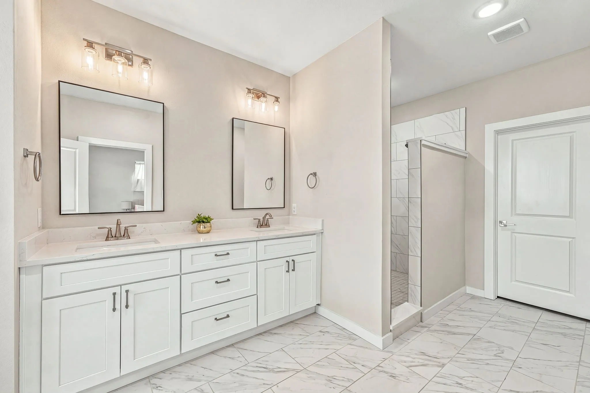 Double vanity featuring white cabinetry, stone-finish countertops, dual rectangular undermount sinks, and wall-mounted vanity lighting, accompanied by a tiled walk-in shower and large-format tile flooring