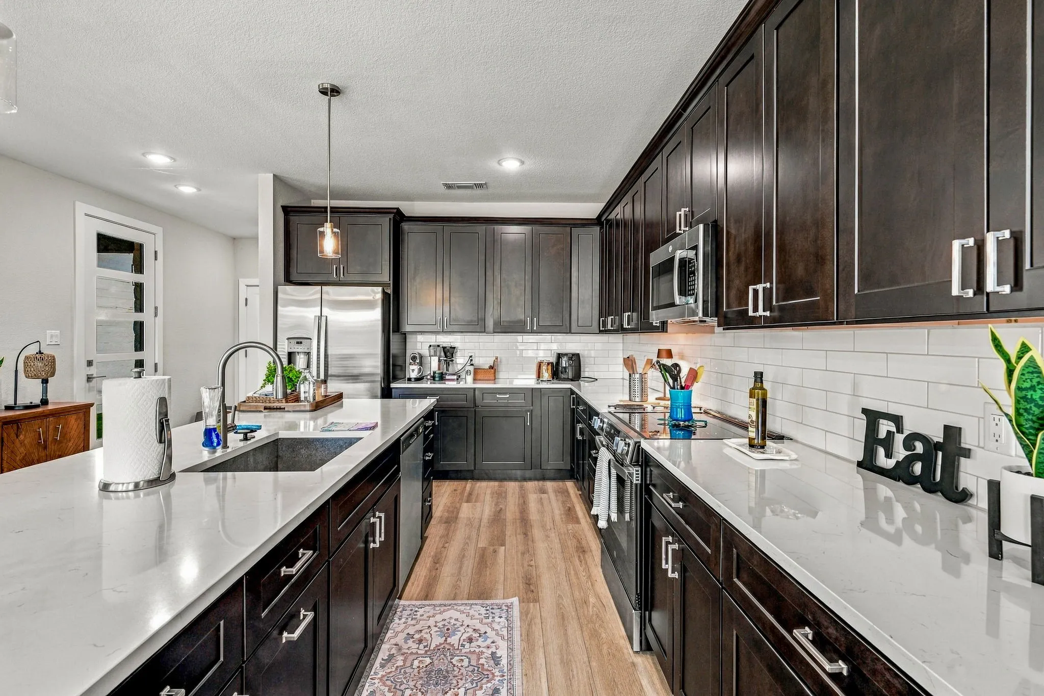 Kitchen featuring dark wood cabinetry, light-toned quartz countertops, a white subway tile backsplash, stainless steel appliances, and wood-finish flooring