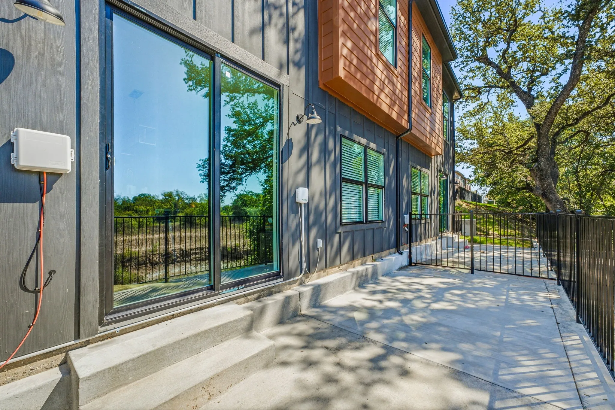 Exterior featuring vertical metal panel siding, horizontal wood-finish siding, sliding glass doors, concrete patio, and metal perimeter fencing