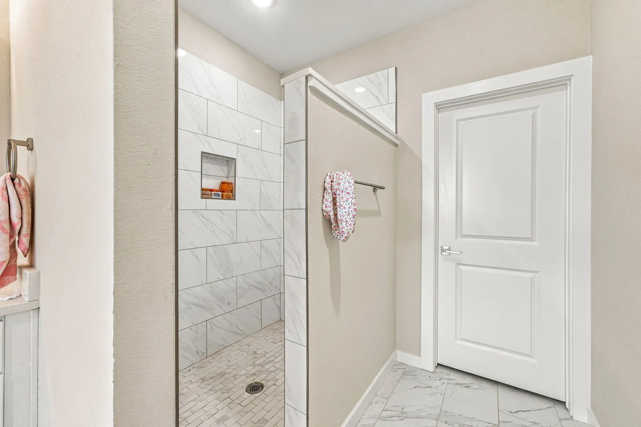 Walk-in shower featuring large-format stone-pattern tile, a built-in recessed wall niche, and stone-pattern tile flooring