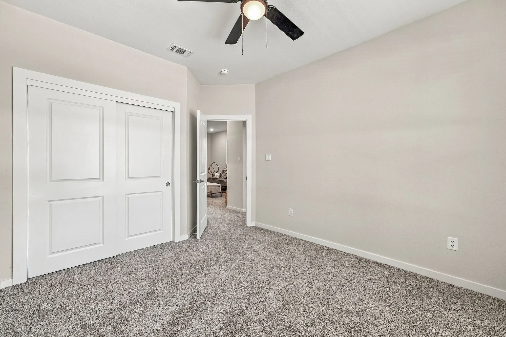 Neutral-toned interior featuring wall-to-wall carpeting, dual-panel sliding closet doors, and a ceiling-mounted light fixture with a fan