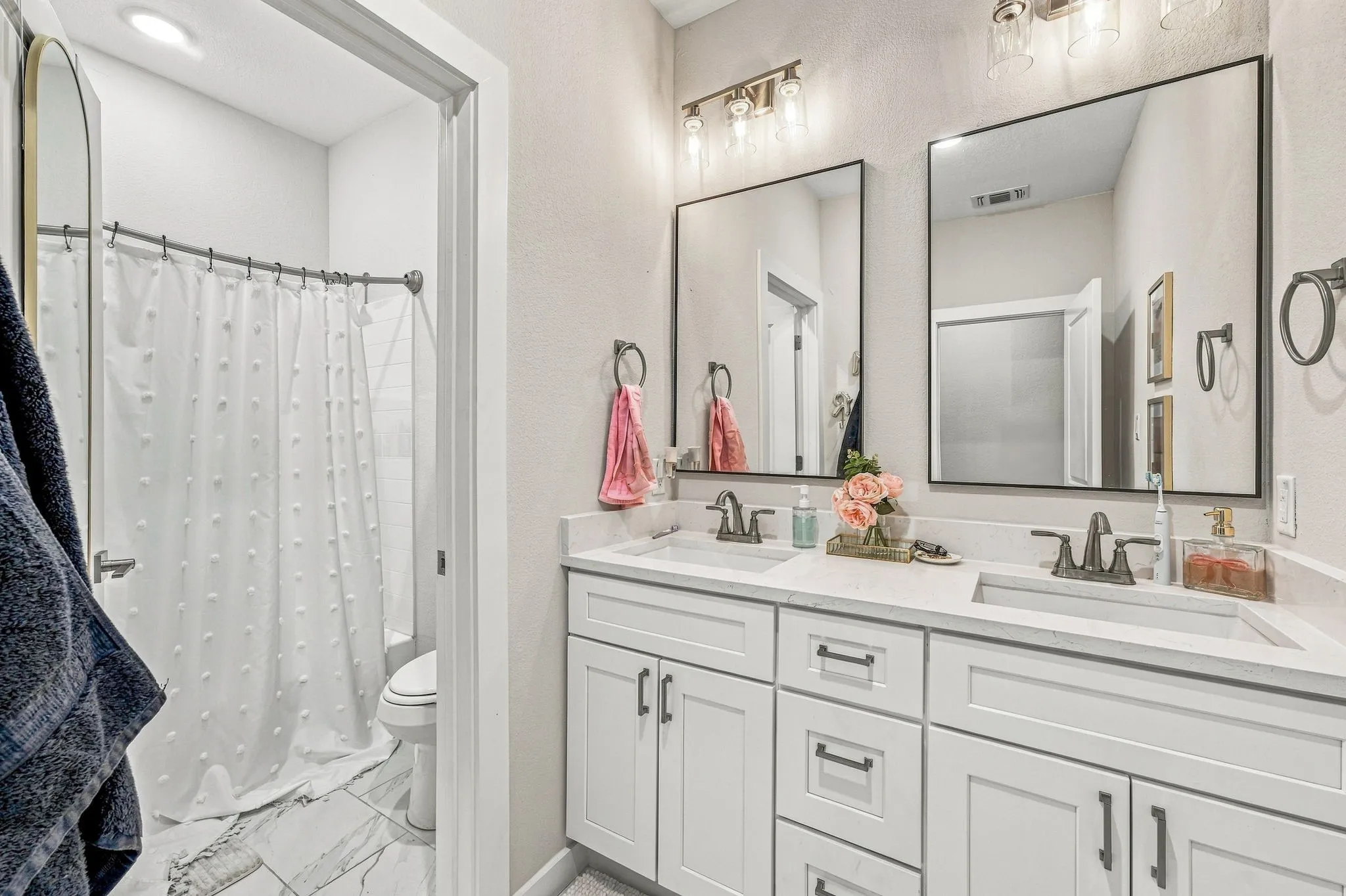 Dual-sink vanity with white shaker-style cabinetry, rectangular undermount sinks, solid-surface countertops, and rectangular mirrors with black frames