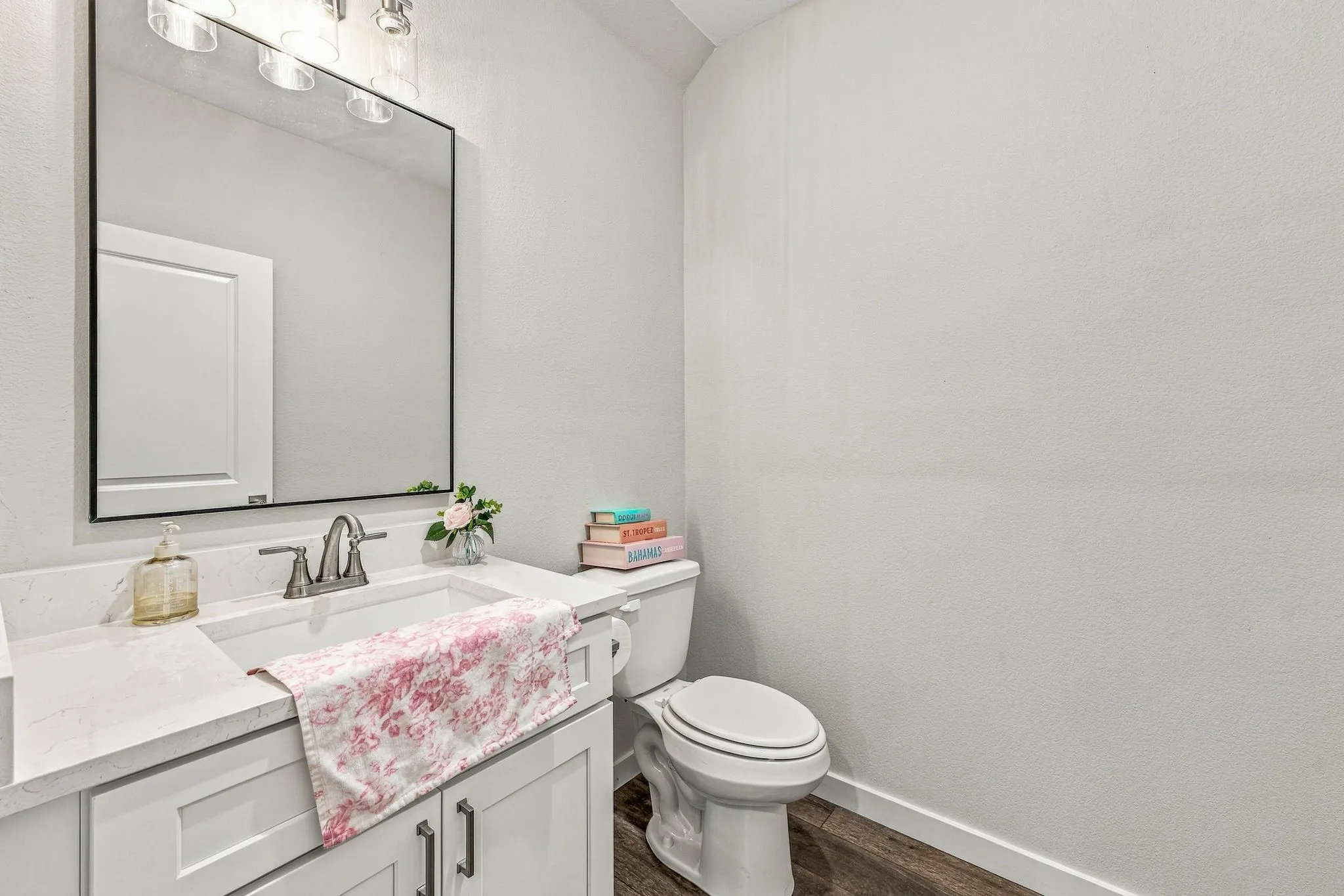 White vanity cabinet featuring a solid-surface countertop with an integrated basin, high-arc chrome faucet, rectangular wall-mounted mirror, and wood-finish flooring