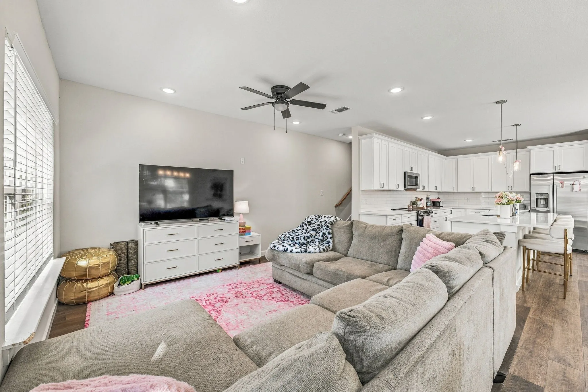 Open-concept living space featuring wood-finish flooring, recessed lighting, ceiling fan, and white cabinetry with stone-surfaced countertops and kitchen island